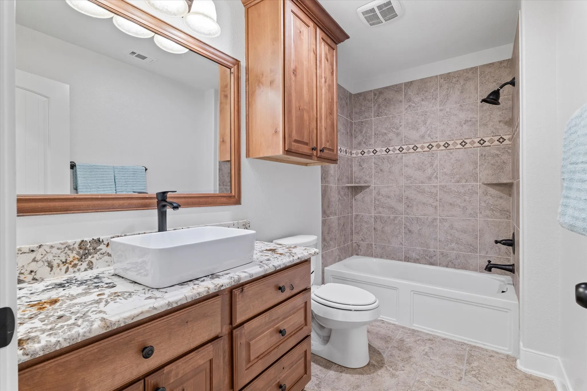 Granite-style countertop with a rectangular vessel sink, wood vanity with drawer storage, tiled shower with integrated shelving, and a built-in bathtub
