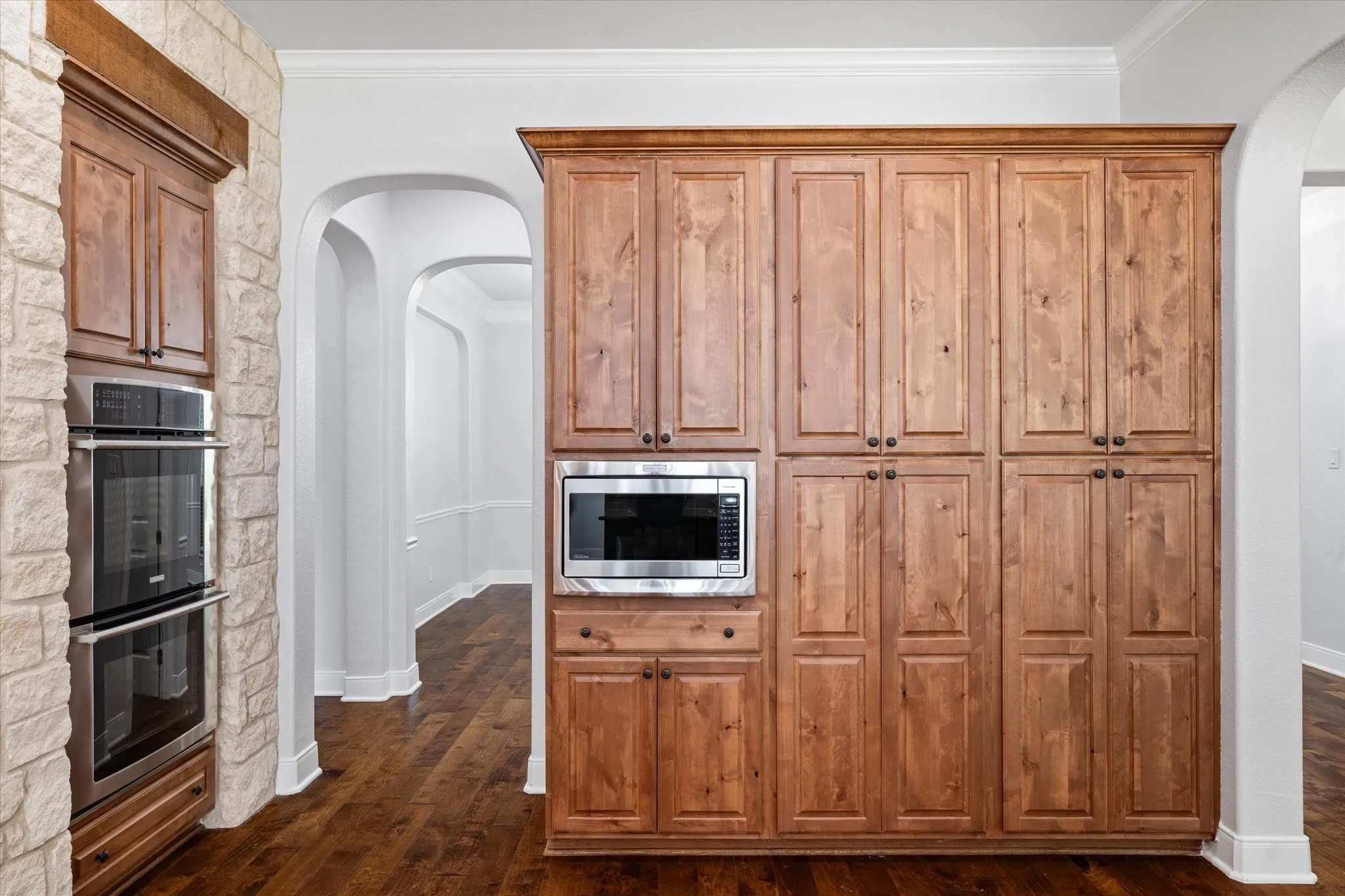 Built-in double ovens, microwave, custom wood cabinetry, stone accent wall, and wood-finish flooring