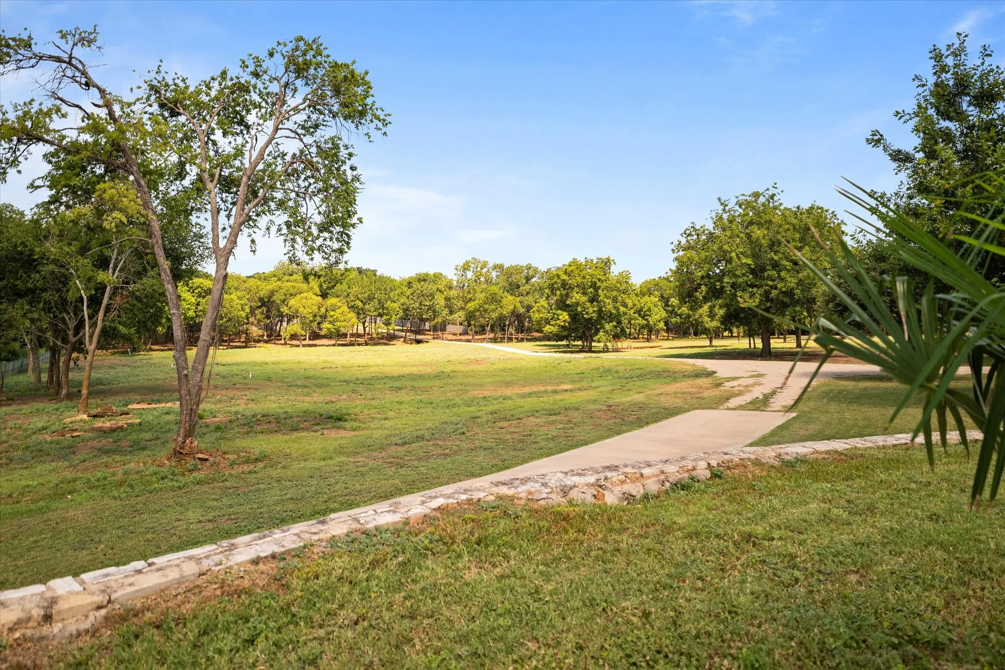 Expansive grassy area with mature trees and a paved pathway