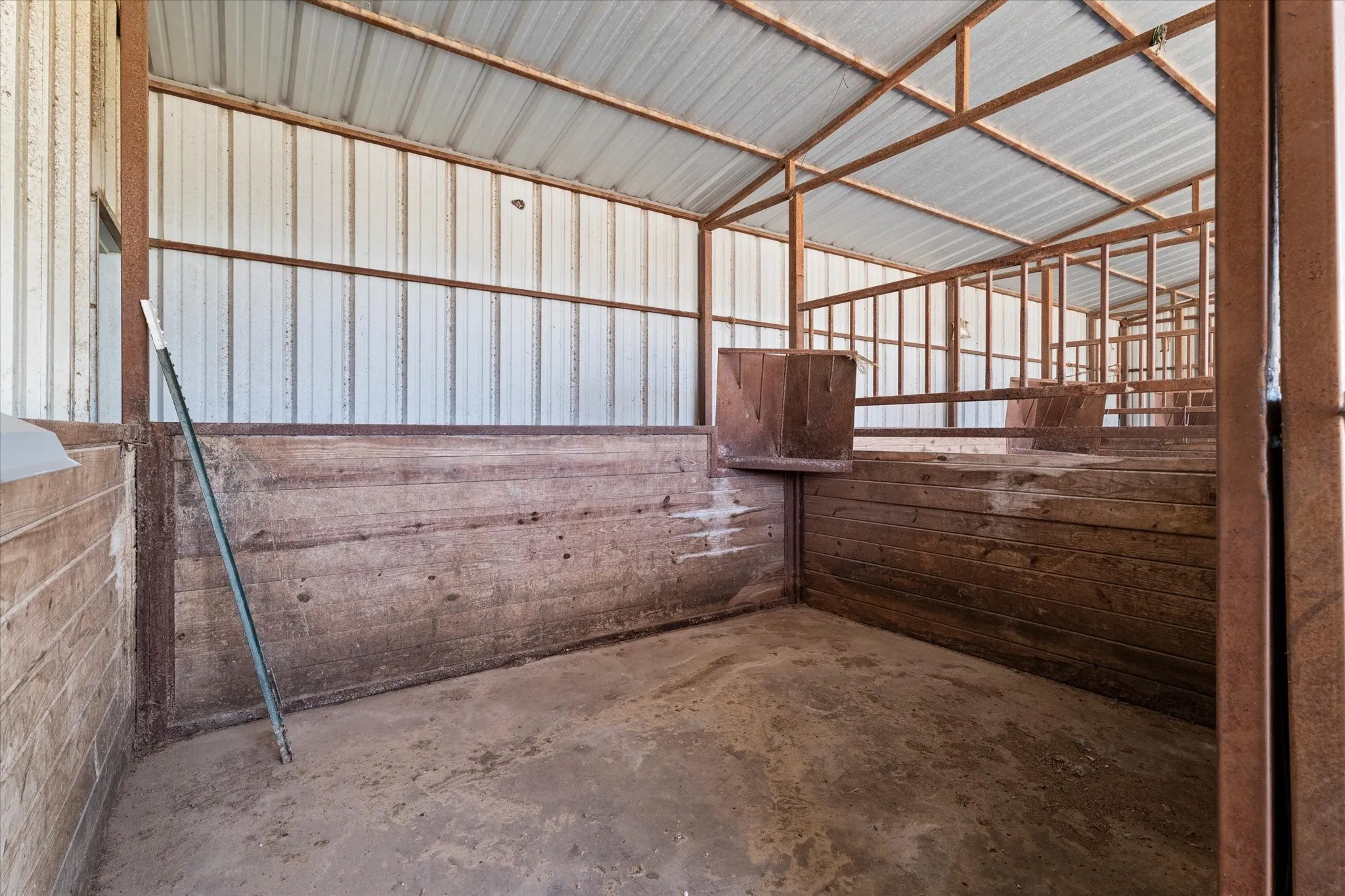 Interior barn structure featuring a corrugated metal roof, metal beam framing, and wood-paneled stalls