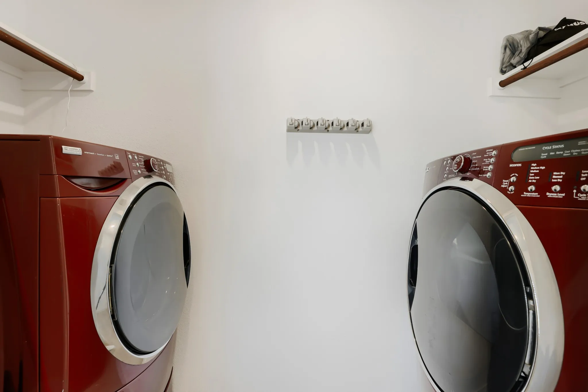 Laundry area featuring a front-loading washer and dryer, wall-mounted drying rack, and wood-finish shelving
