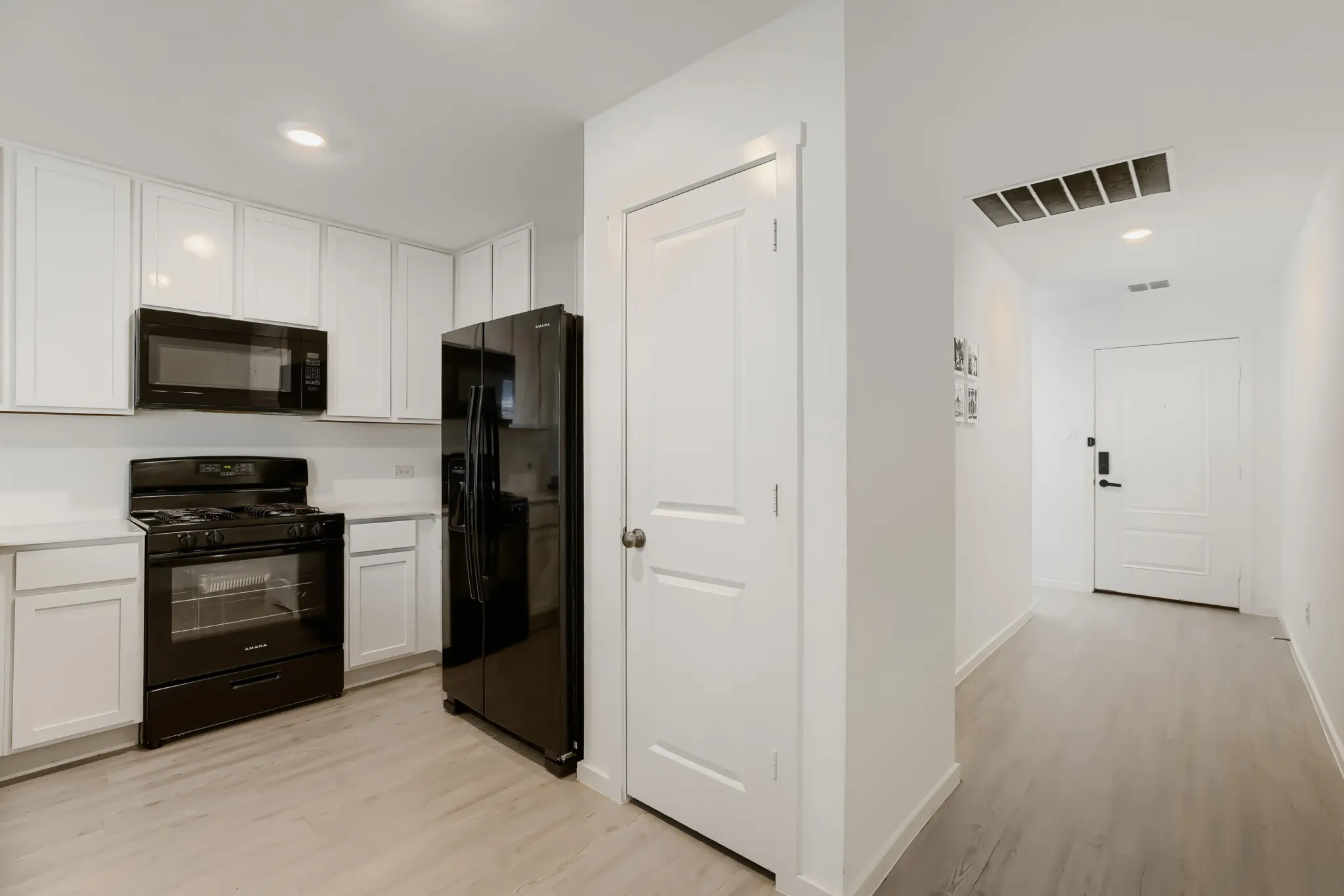 Kitchen featuring white cabinetry, light countertops, black appliances, and wood-finish flooring