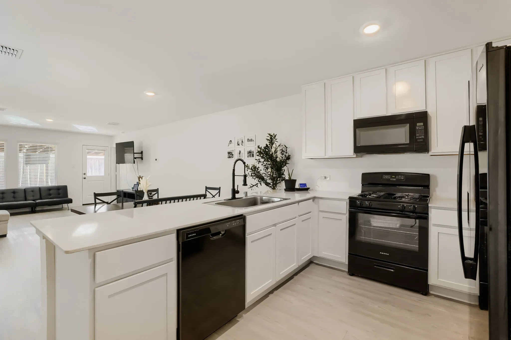 Kitchen featuring white cabinetry, light-toned countertops, black appliances, and wood-finish flooring