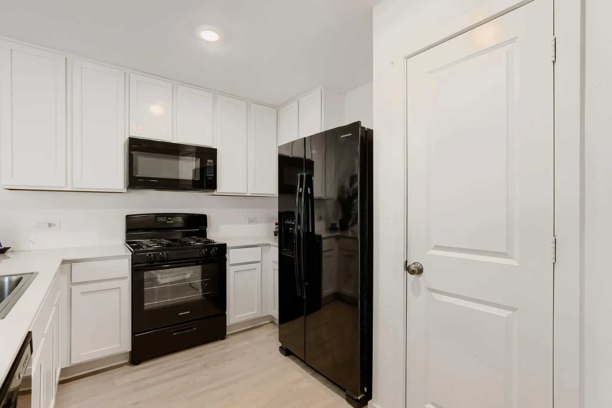 Kitchen featuring white upper and lower cabinetry, light-toned countertops, black appliance suite, and wood-finish flooring
