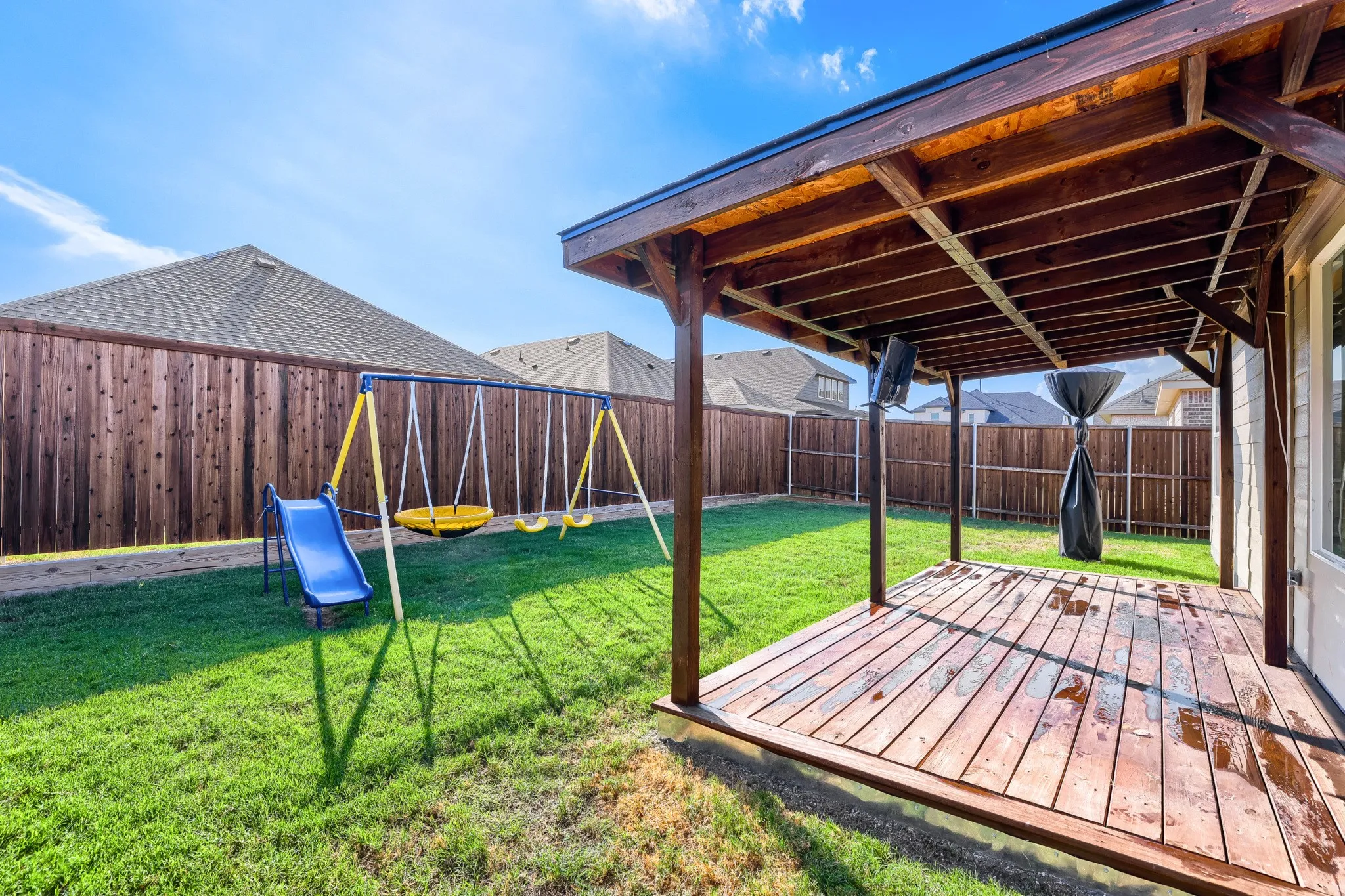 Expansive backyard featuring a covered wood deck, wood privacy fencing, and a manicured lawn