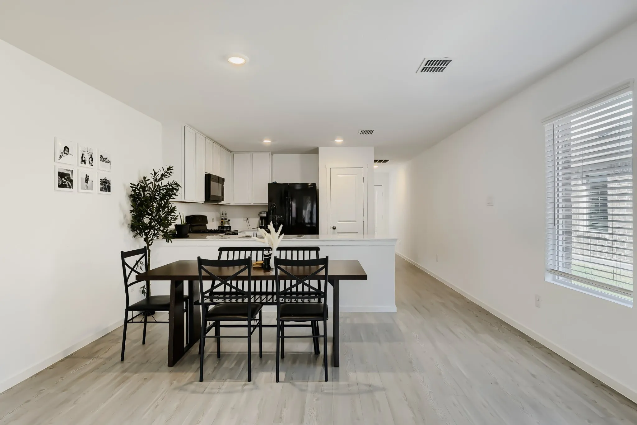 Recessed lighting, wood-finish flooring, white cabinetry, black appliances, and a window with blinds