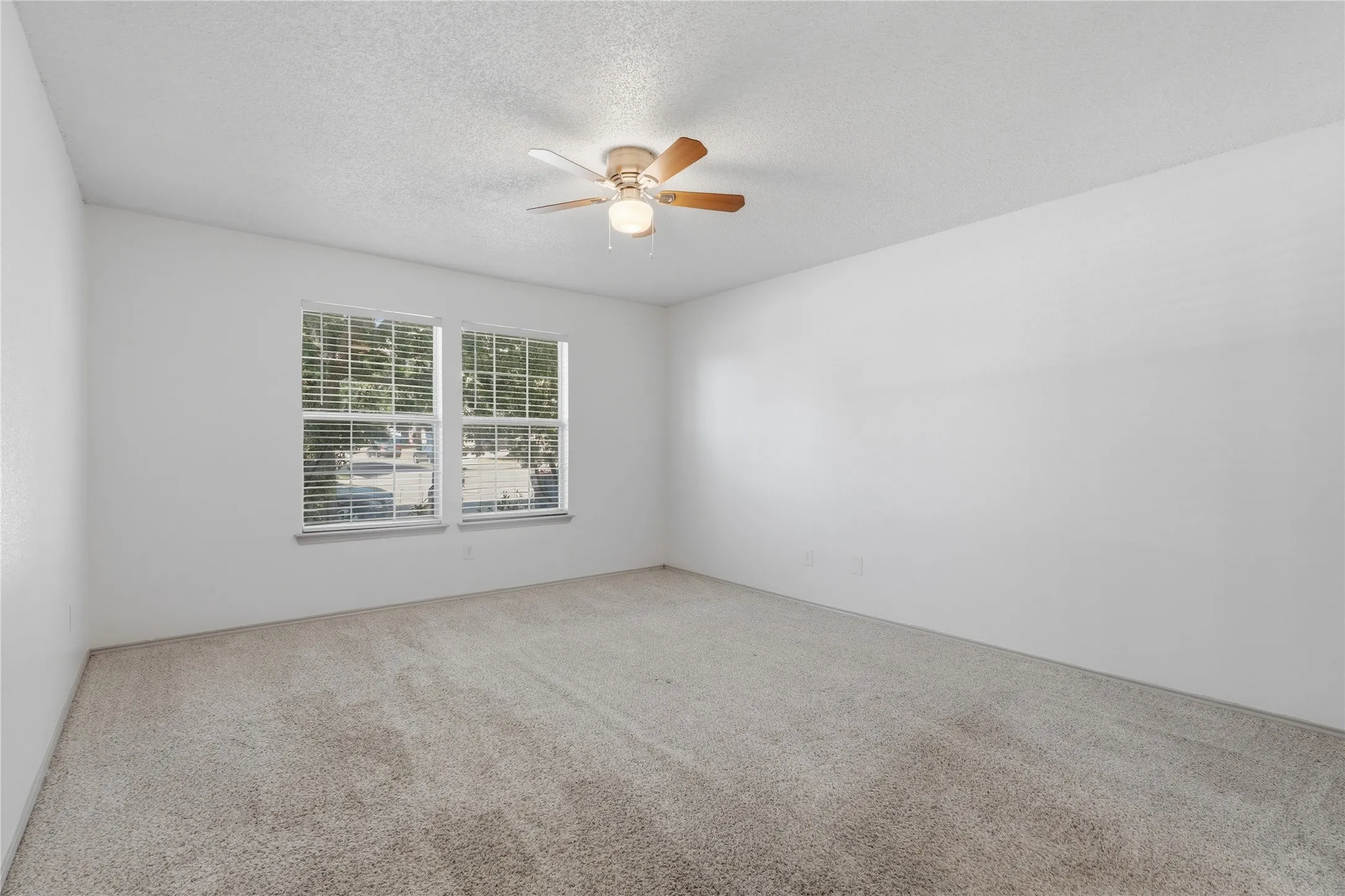 Spacious room featuring neutral carpeting, a ceiling fan with integrated lighting, and two windows