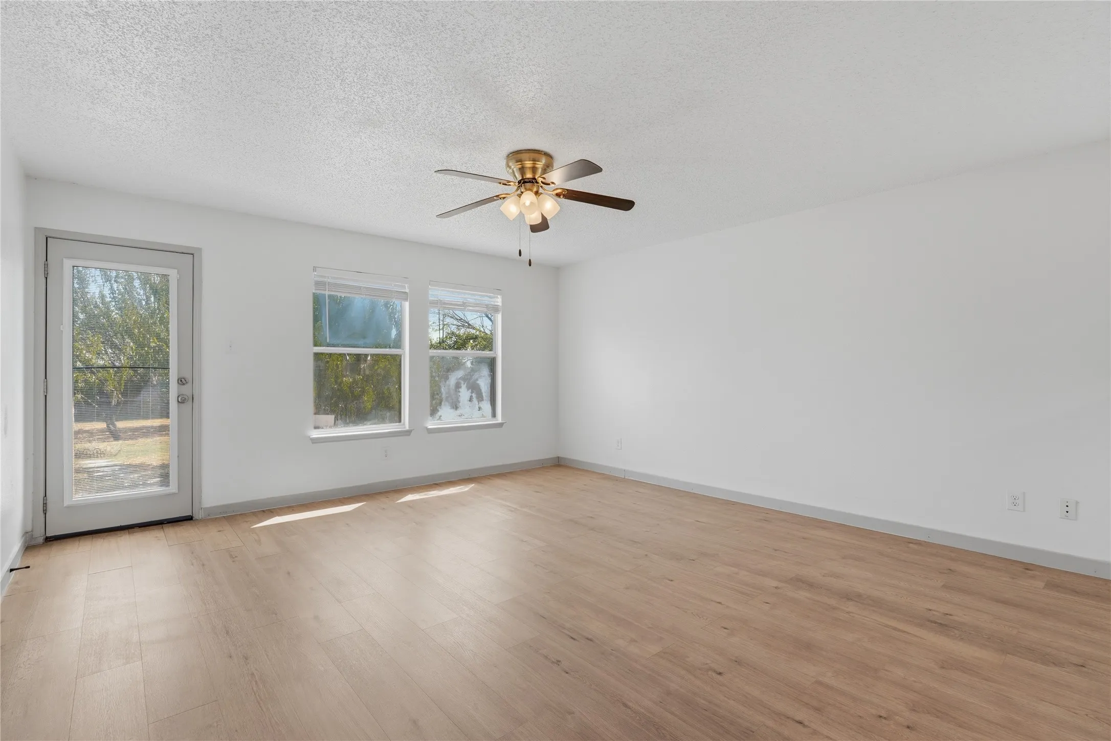 Wood-finish flooring, ceiling fan, multiple windows, and a glass-paneled door