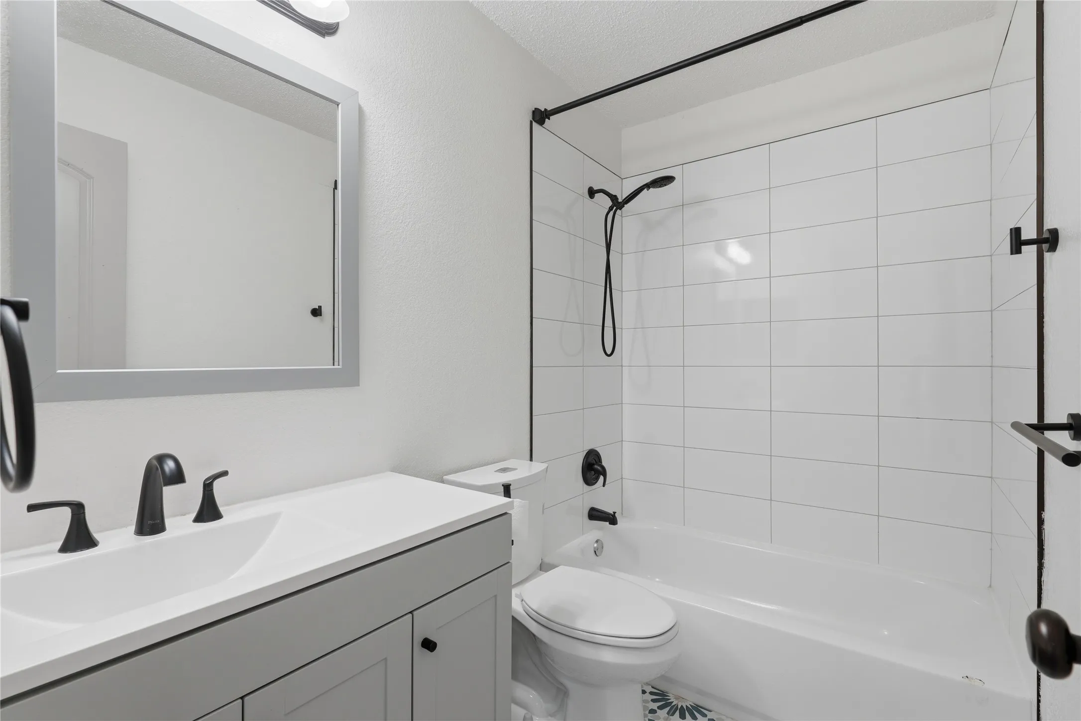 White subway tile shower surround, matte black fixtures, light gray vanity with white countertop, integrated sink, and framed mirror