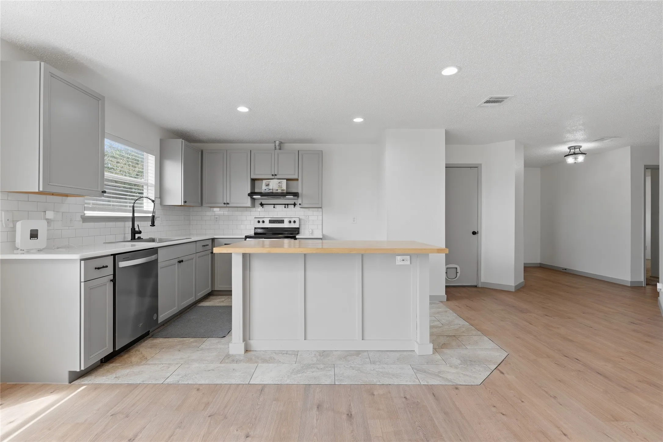 Kitchen featuring light gray cabinetry, white subway tile backsplash, a built-in dishwasher, and wood-finish flooring