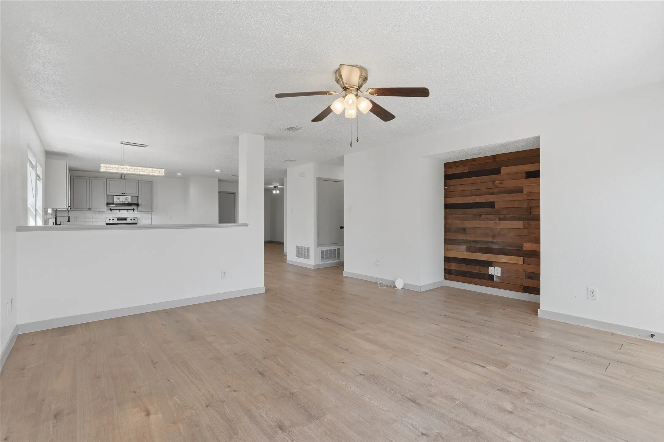Light wood-finish flooring throughout, a decorative wood-paneled accent wall, and a ceiling fan with integrated lighting