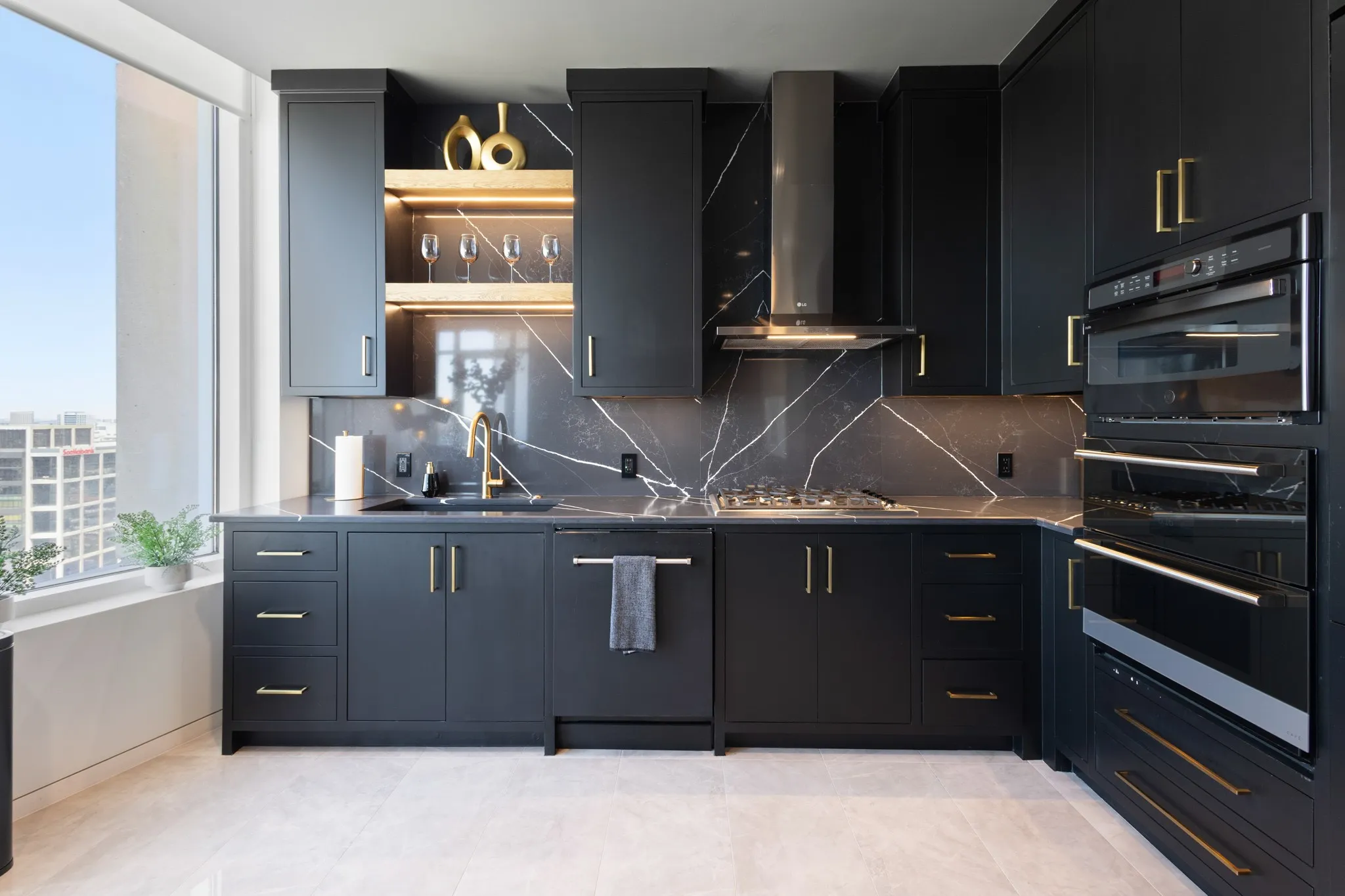 Modern kitchen featuring black cabinetry with gold-tone hardware, a dark marble-patterned backsplash, and a built-in oven and microwave