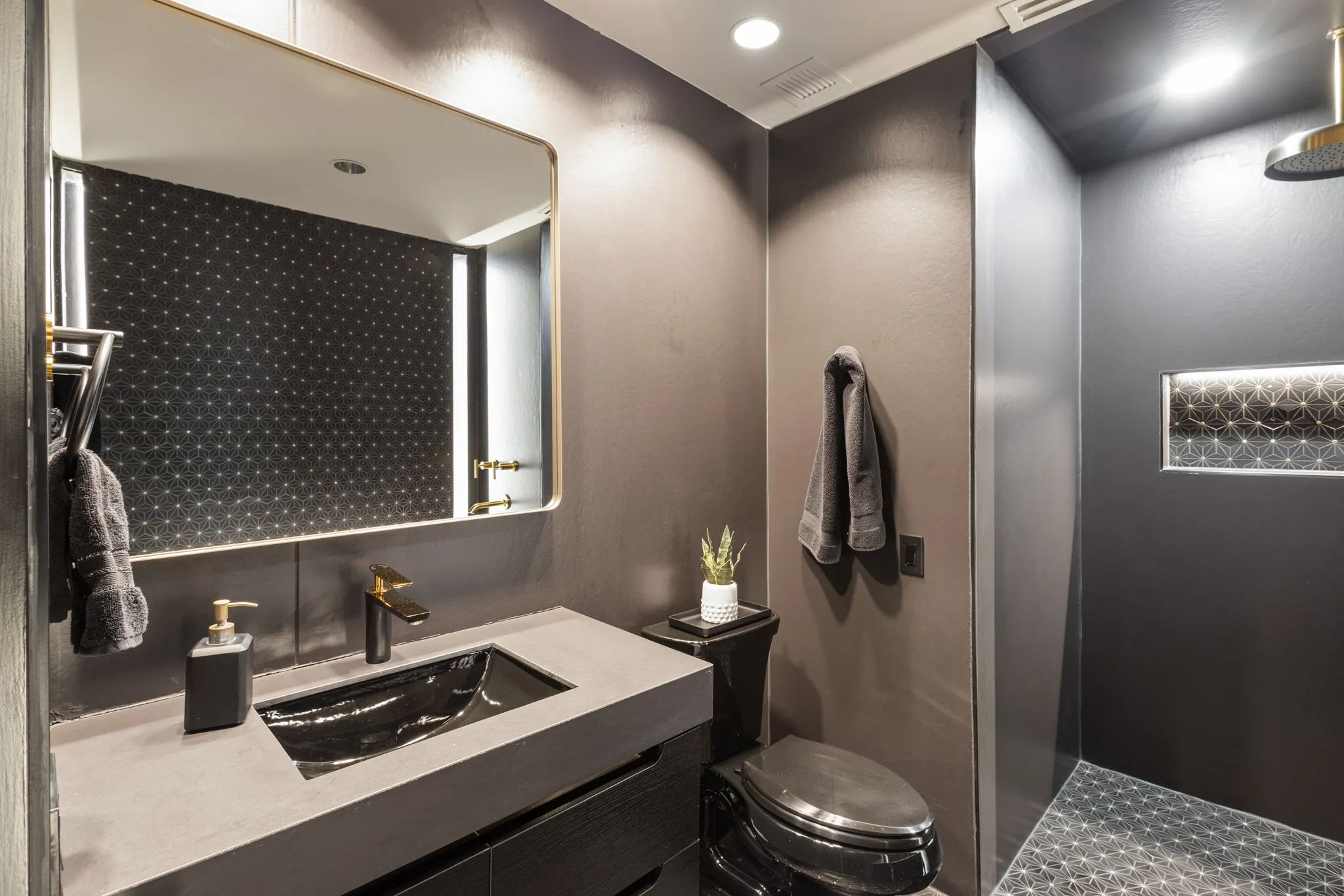 Vanity with an integrated black sink and gold-tone faucet, complemented by a gold-framed mirror