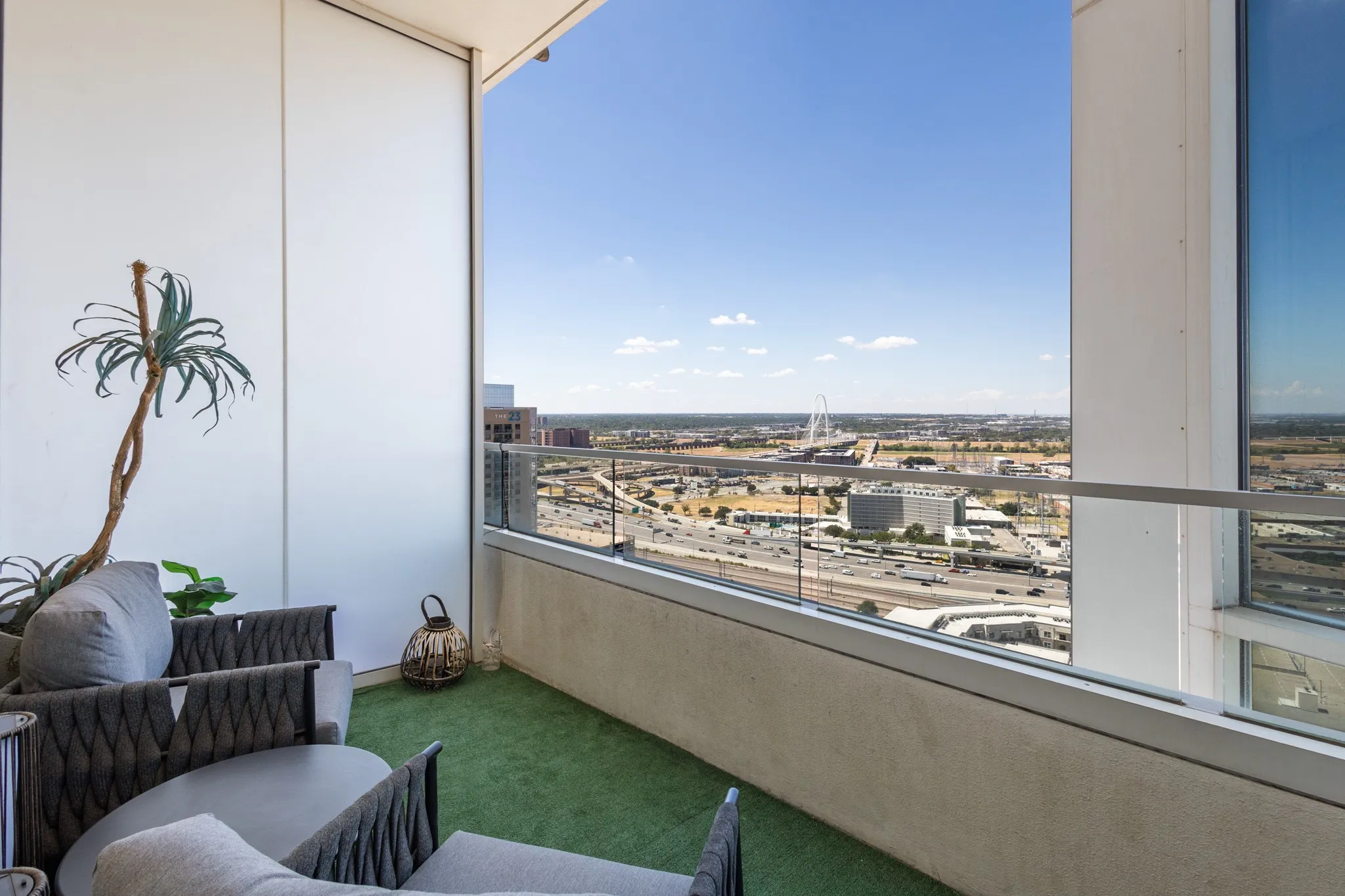 Balcony with glass railing, turf-covered flooring, and surrounding cityscape