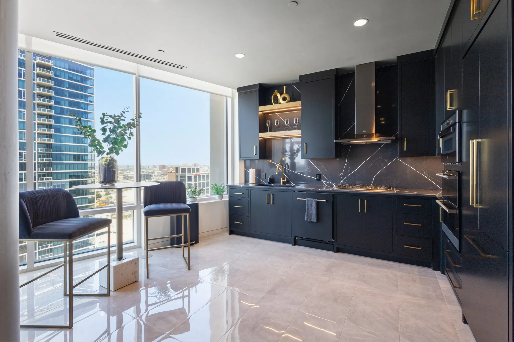 Sleek kitchen featuring dark cabinetry, integrated appliances, gold-finish hardware, a full-height backsplash with veining, and a gas cooktop