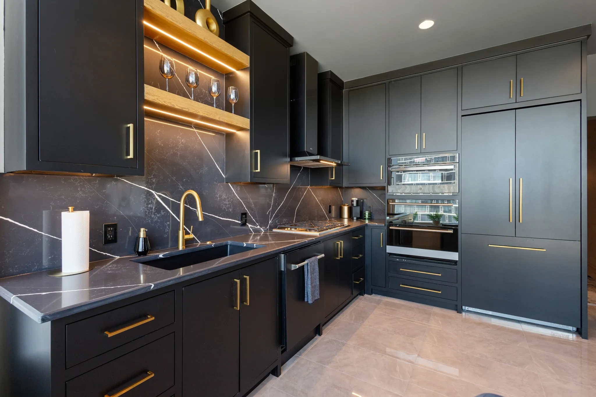 Sleek kitchen featuring dark cabinetry, gold-tone hardware, integrated appliances, and a dramatic veined countertop and backsplash