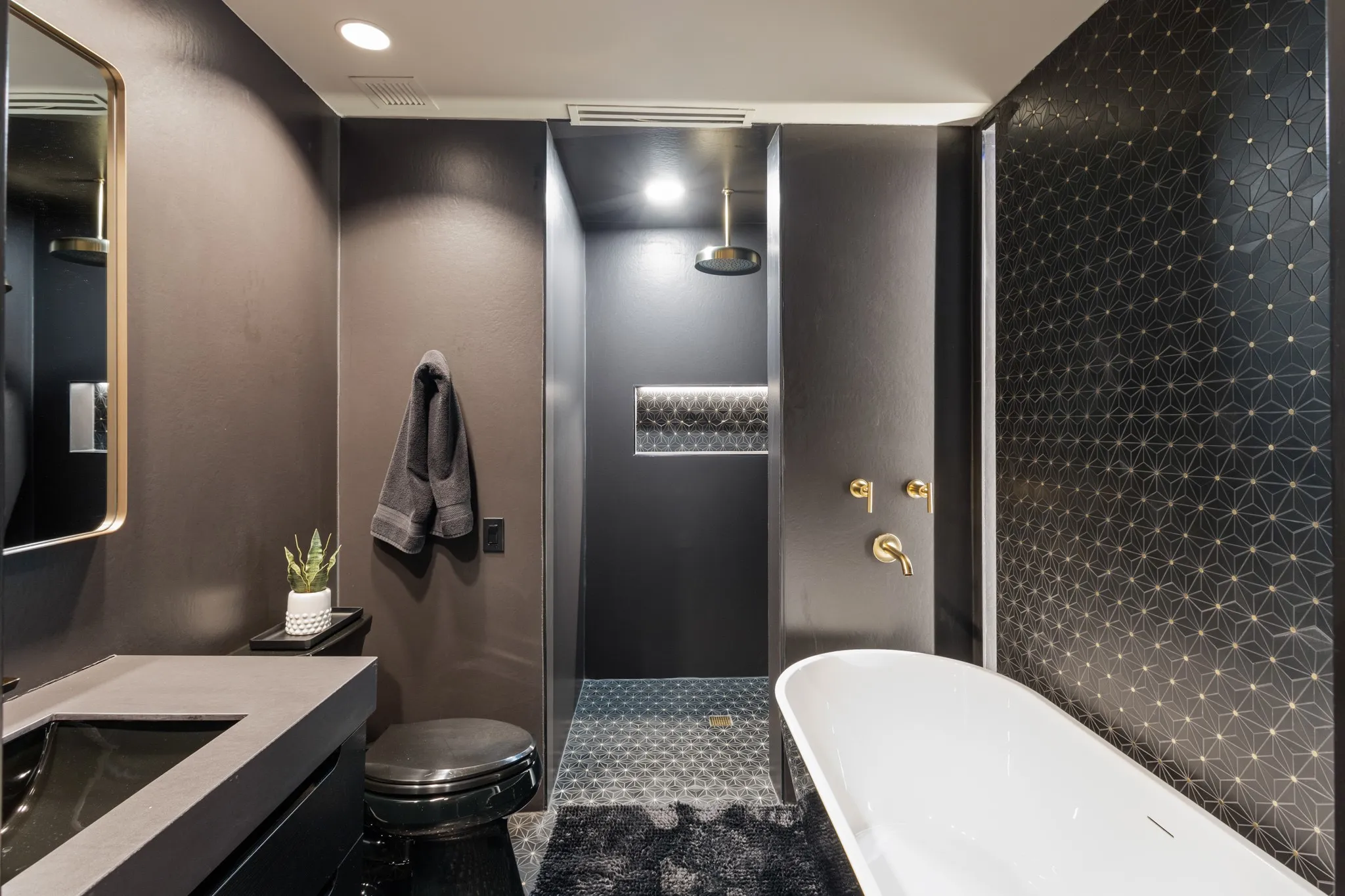 Freestanding soaking tub with brass fixtures, a geometric patterned accent wall, and a large walk-in shower with a rainfall showerhead