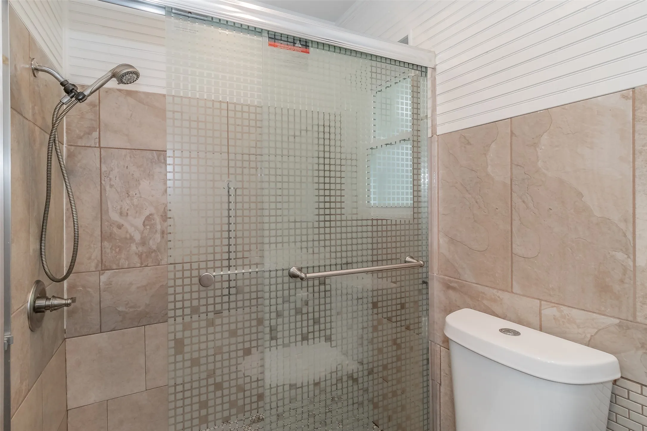 Enclosed shower with patterned glass doors, a handheld showerhead, and tile surround