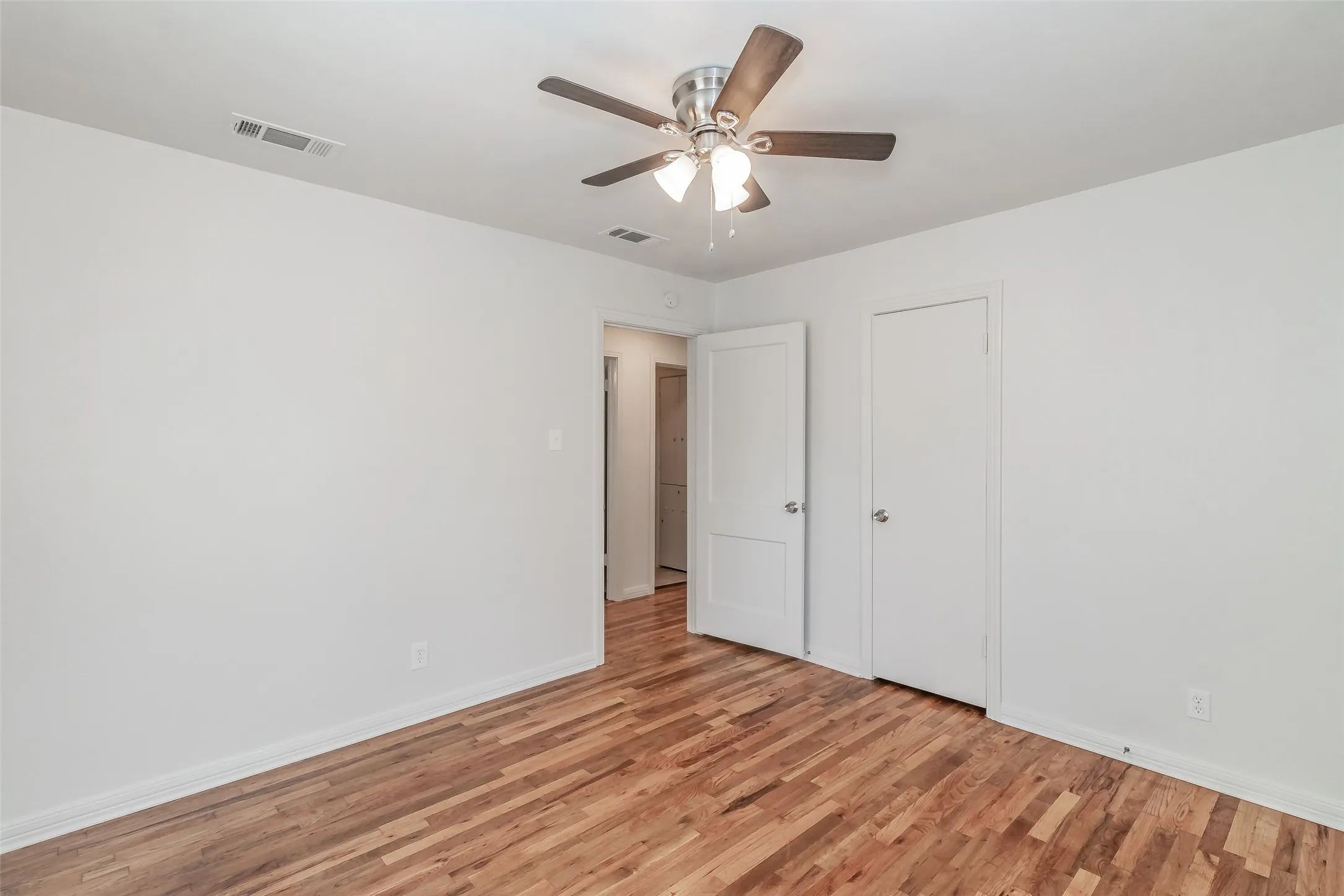 Wood-finish flooring with white walls, featuring a ceiling fan with integrated lighting and white interior doors