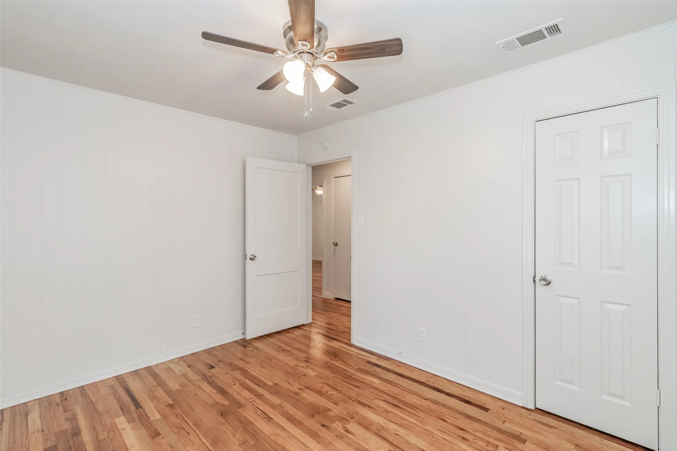 Wood-finish flooring, white paneled doors, ceiling fan with integrated lighting, and white walls