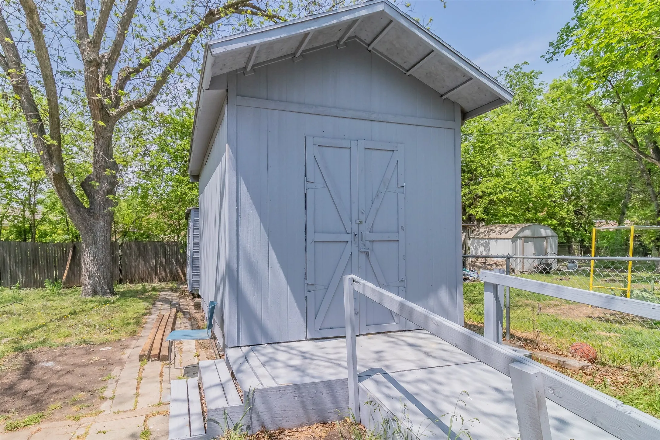 Exterior storage shed featuring a ramp entrance, double barn doors, and mature trees