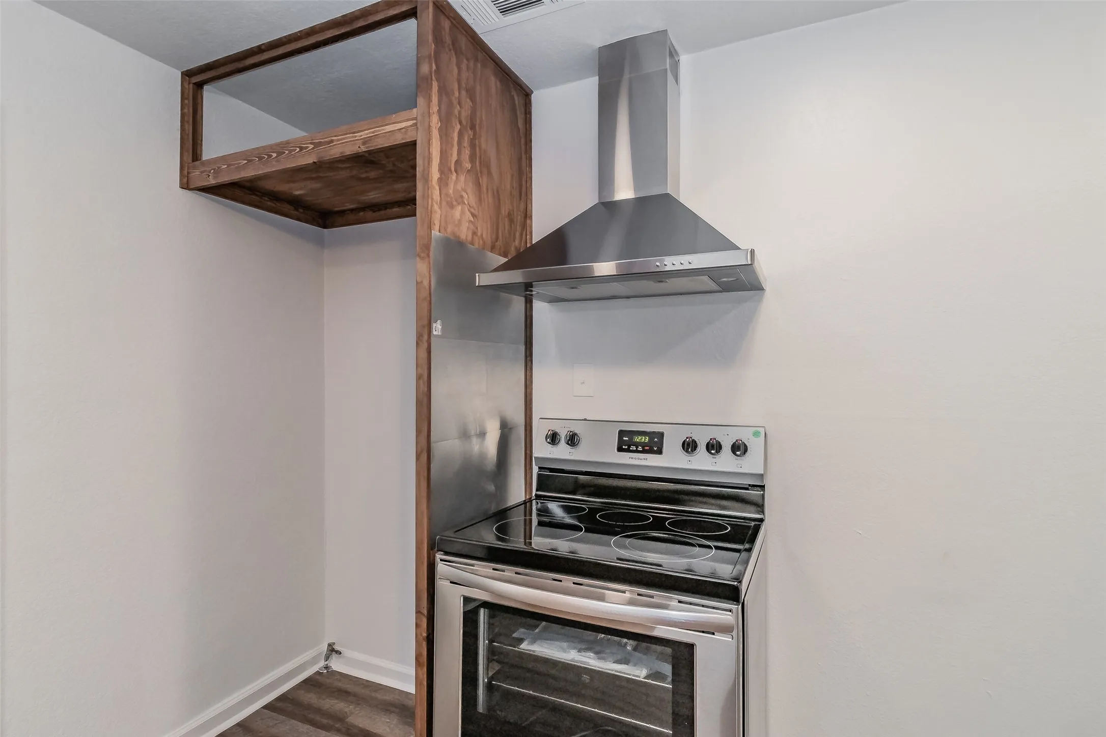 Stainless steel electric range with a black ceramic cooktop, stainless steel range hood, and wood-finish open shelving
