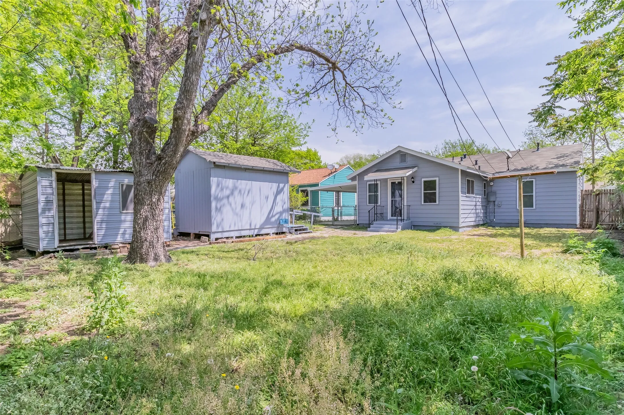 Rear exterior with siding, two storage sheds, a mature tree, and a covered porch