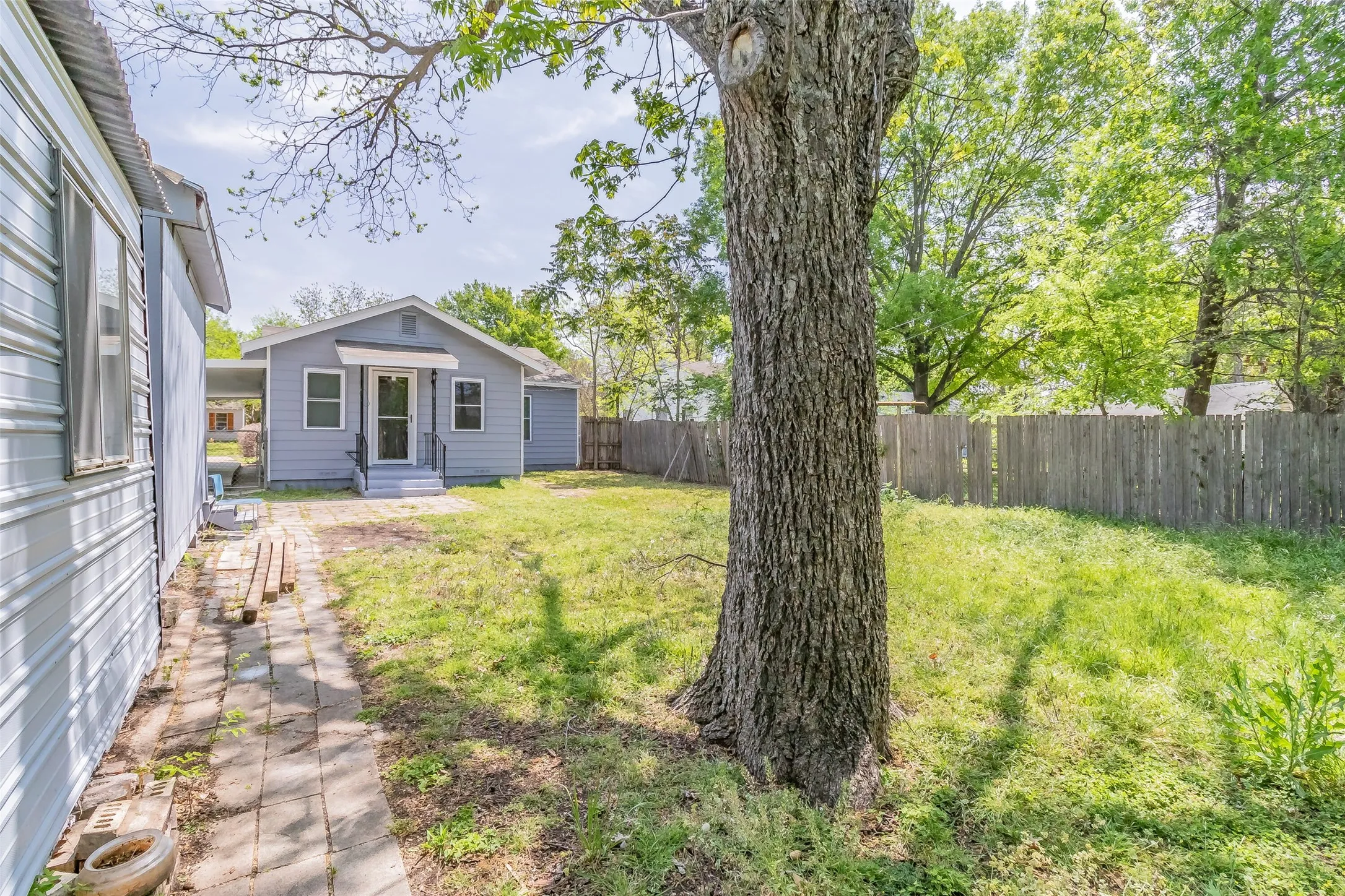 Fenced backyard featuring mature trees, a brick paver pathway, and a detached structure with horizontal siding