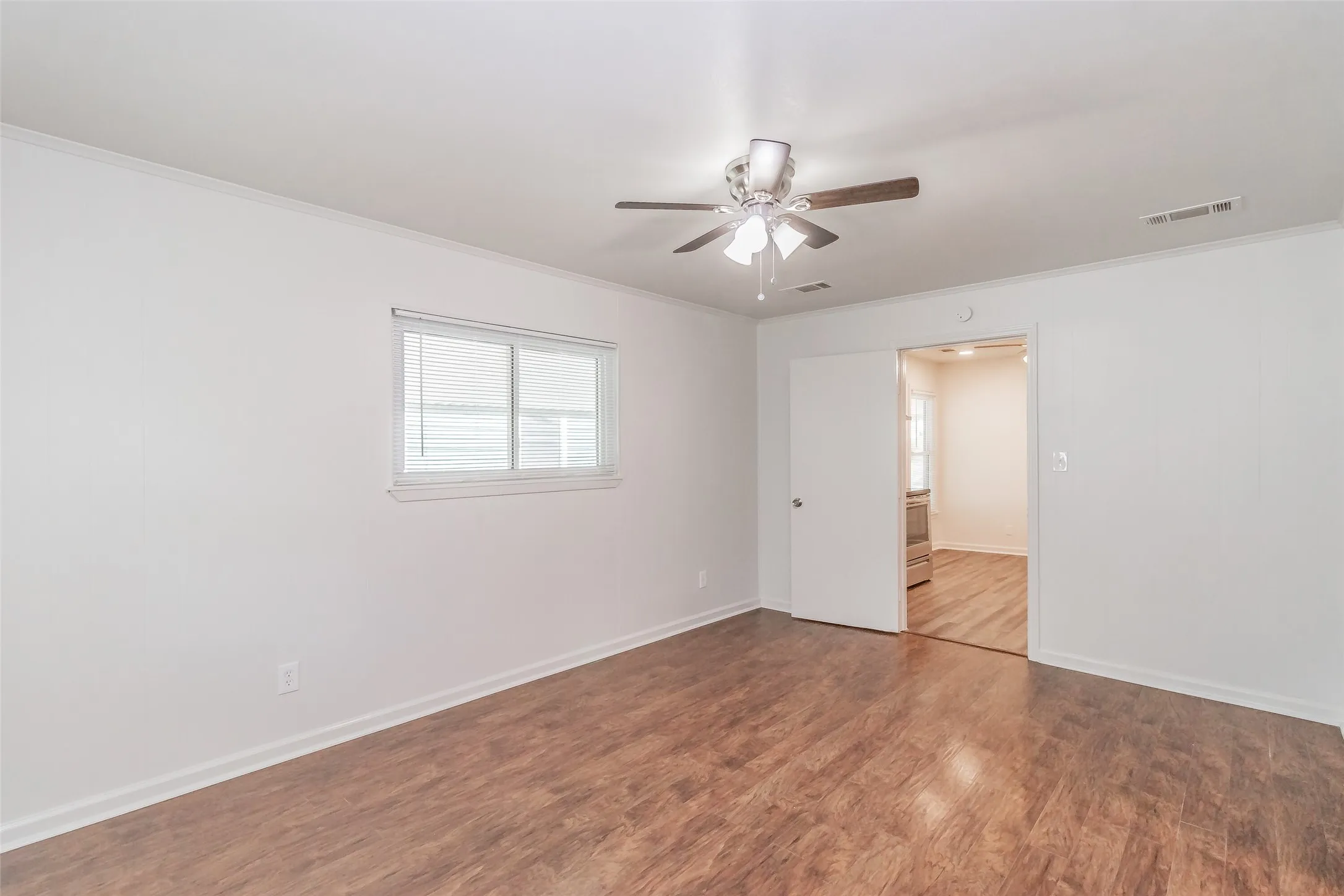 Wood-finish flooring, ceiling fan with light fixture, white interior walls, and window with blinds