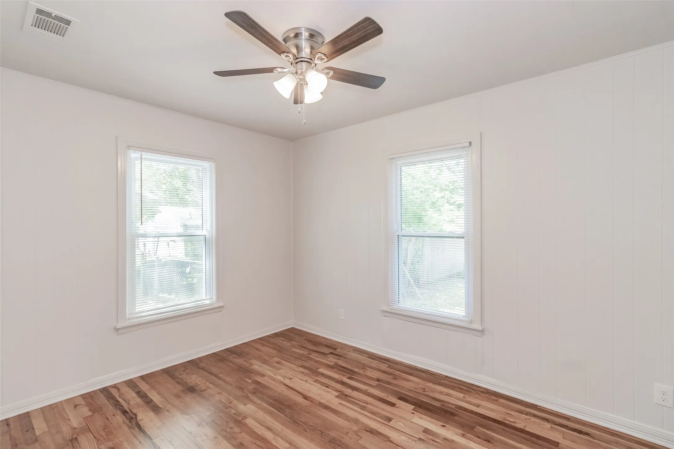 Wood-finish flooring, two windows with blinds, and a ceiling fan with integrated lighting