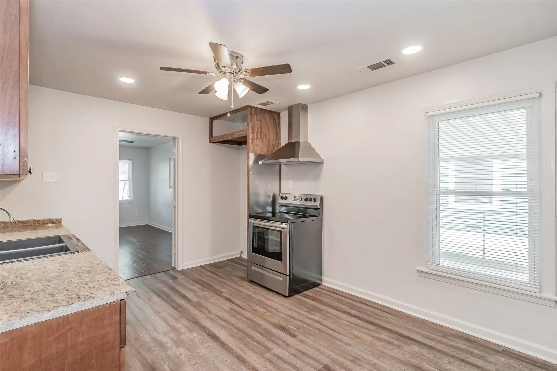 Stainless steel range with matching range hood, wood-finish flooring, recessed lighting, ceiling fan with light fixture, and stone-look countertops
