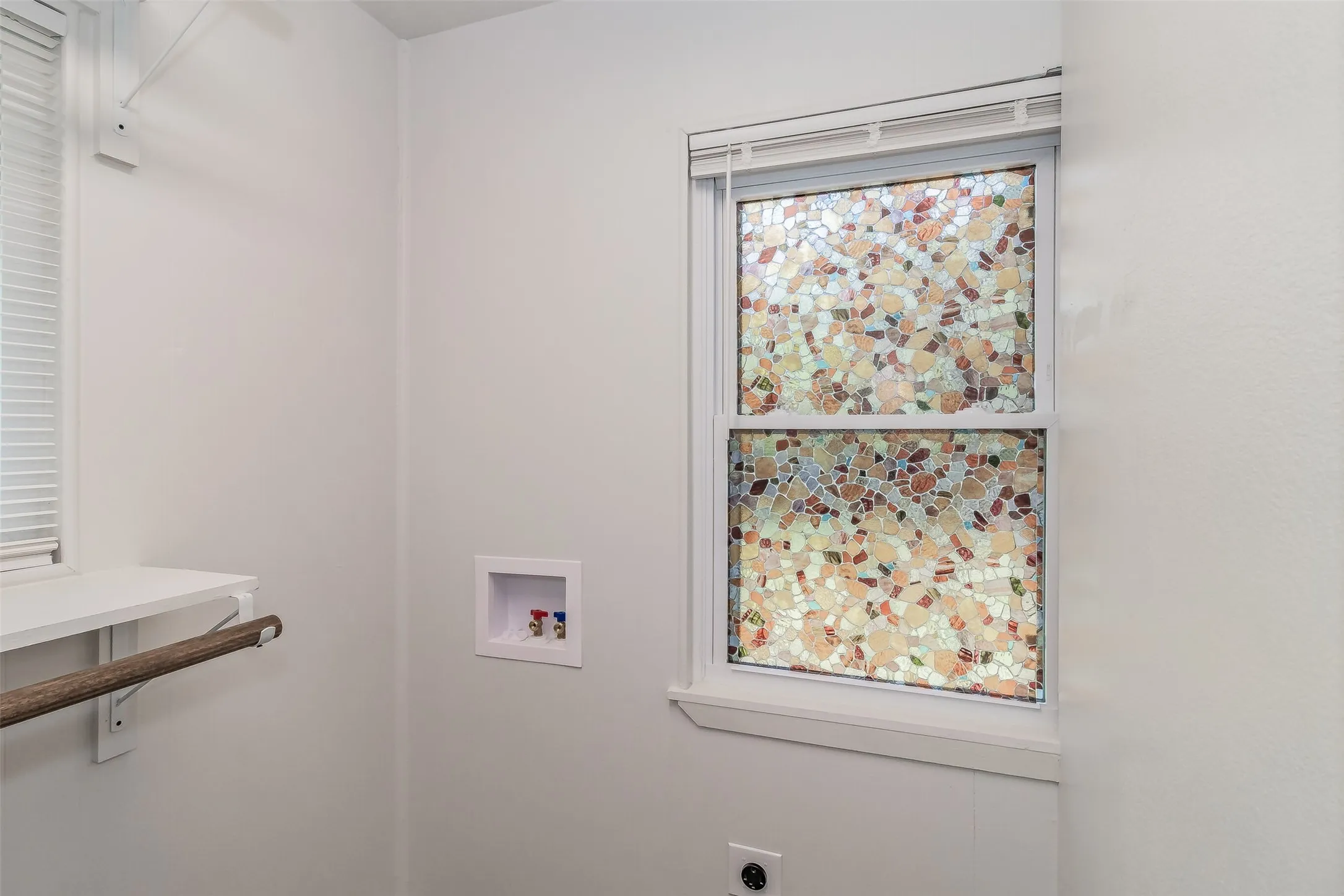 Utility connections, white walls, window with decorative film, wall-mounted shelving, and a hanging rod
