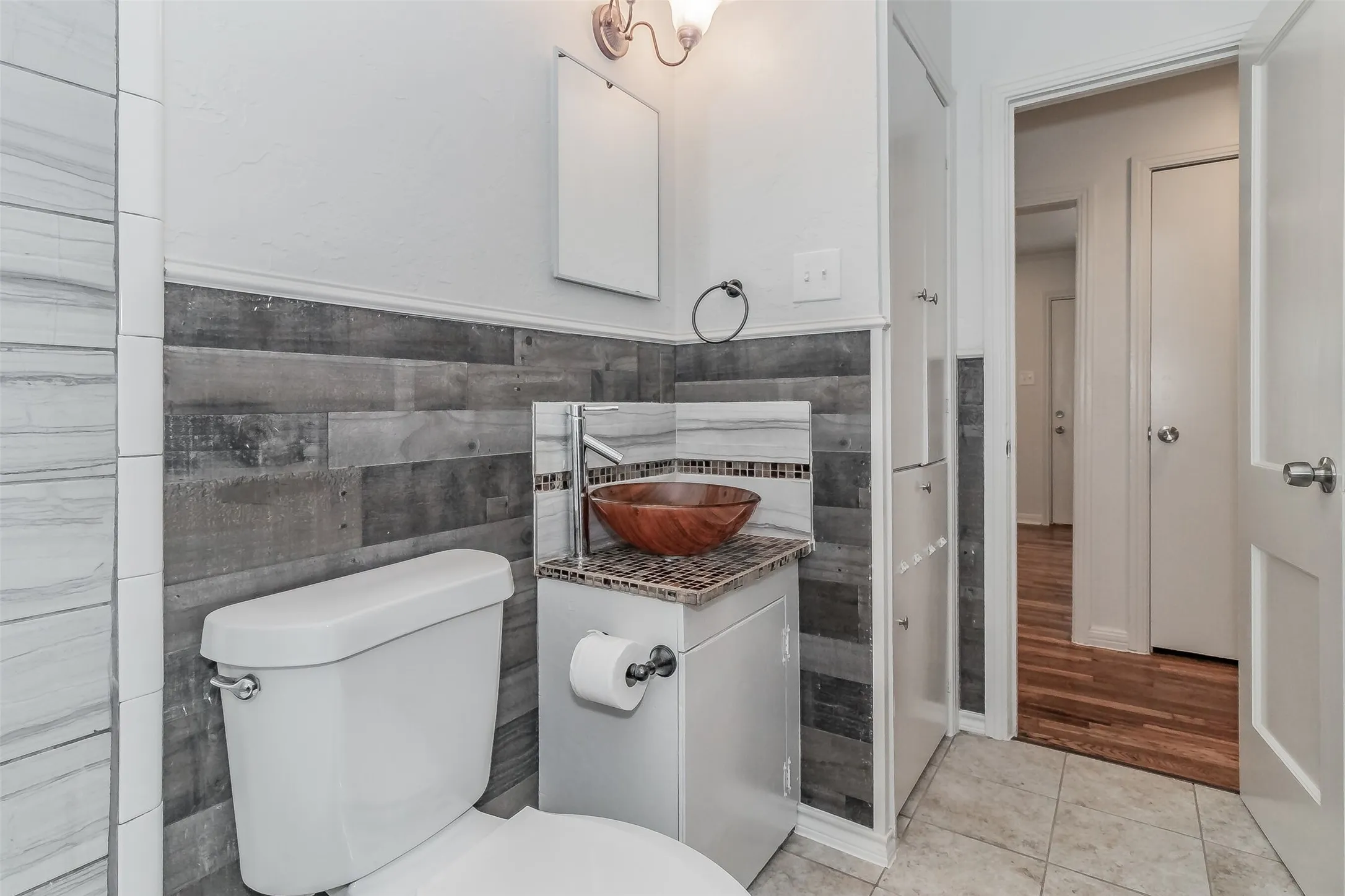 Bathroom featuring a vessel sink with a mosaic tile backsplash, wood-finish wall paneling, and tile flooring