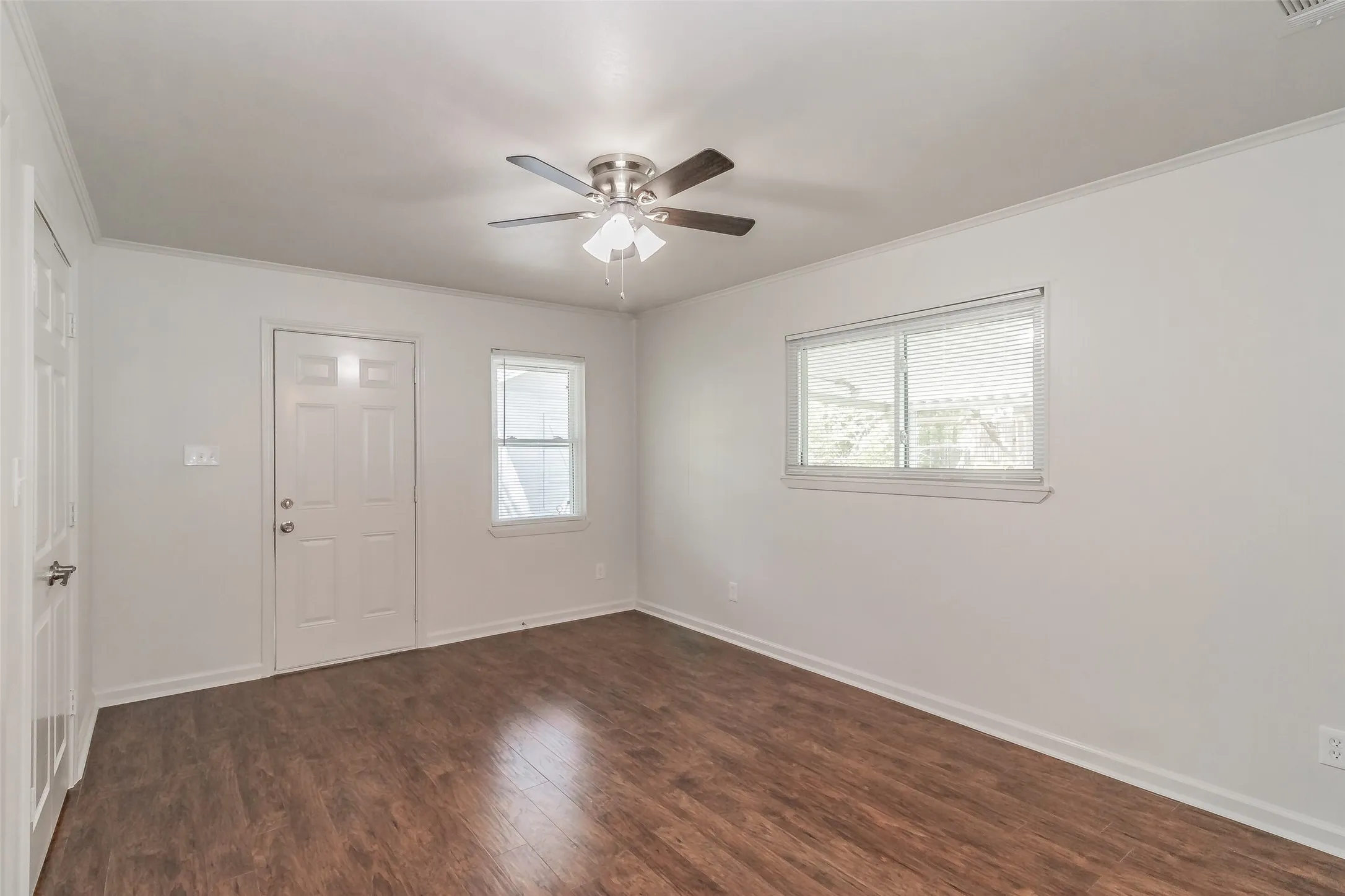 Wood-finish flooring with white trim, a ceiling fan with light fixture, and multiple windows