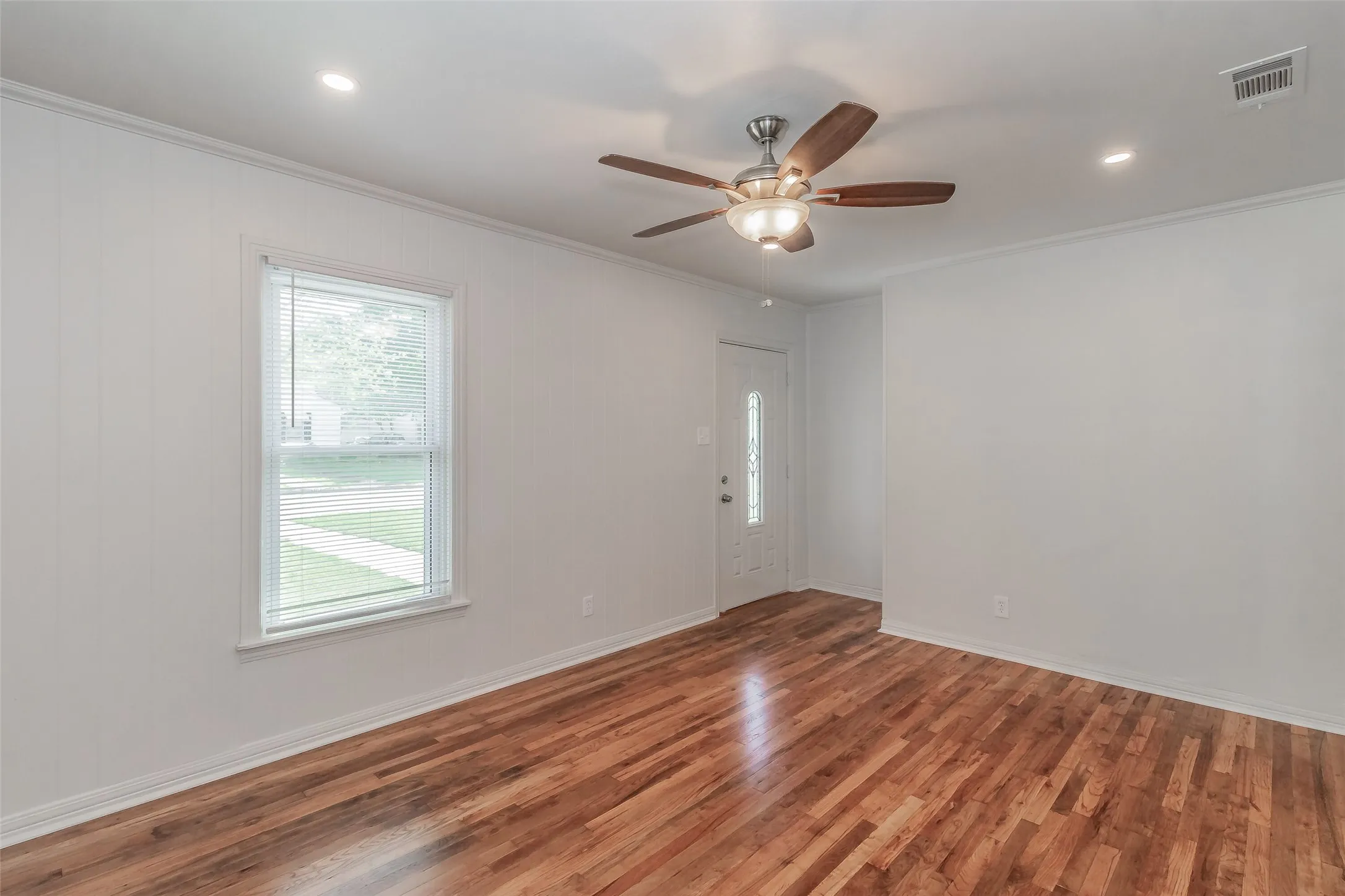 Wood-finish flooring with white paneled walls, a ceiling fan with integrated lighting, recessed lighting, and a front entry door with decorative glass