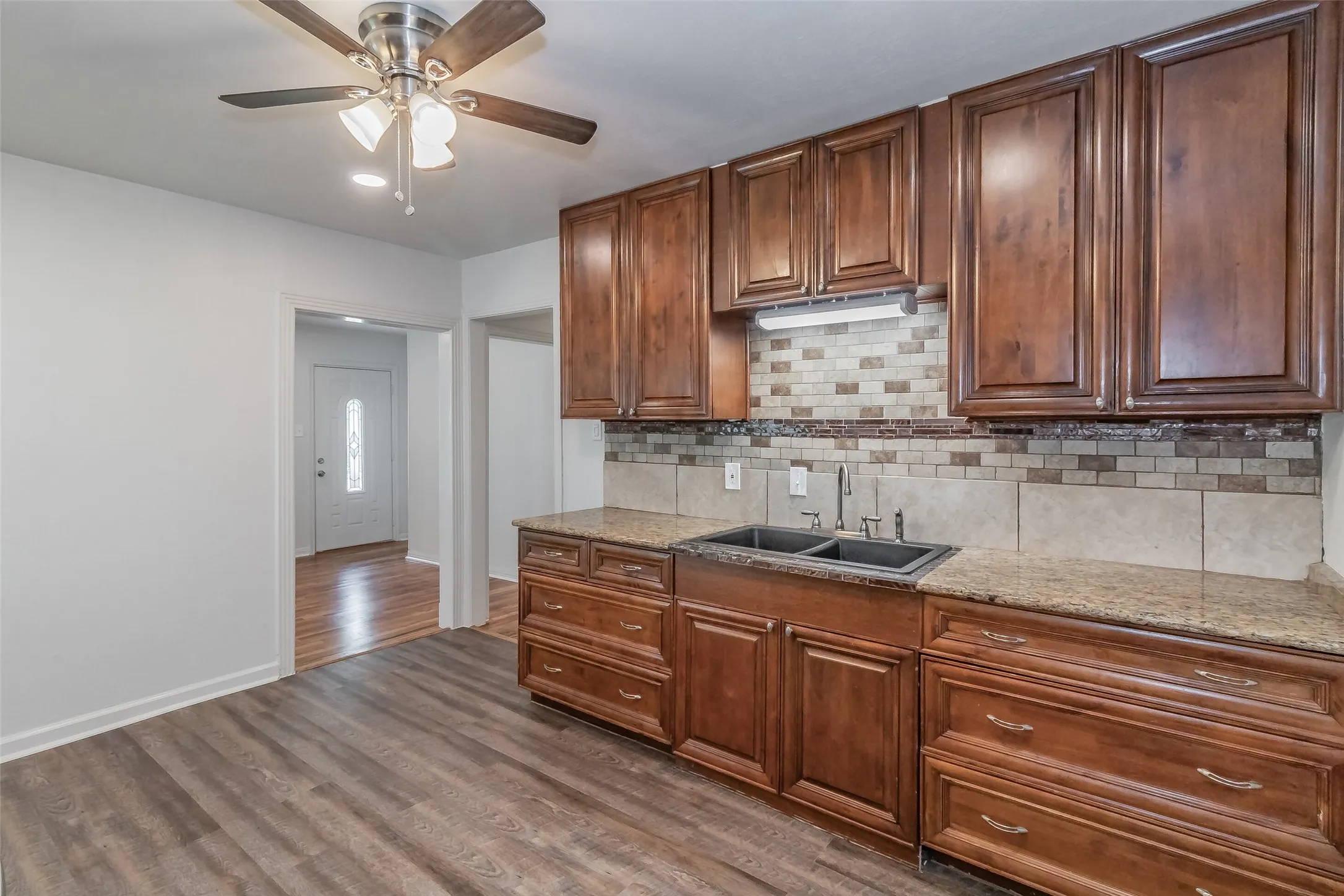 Wood-finish flooring, recessed lighting, ceiling fan, wood cabinetry, and a double basin sink