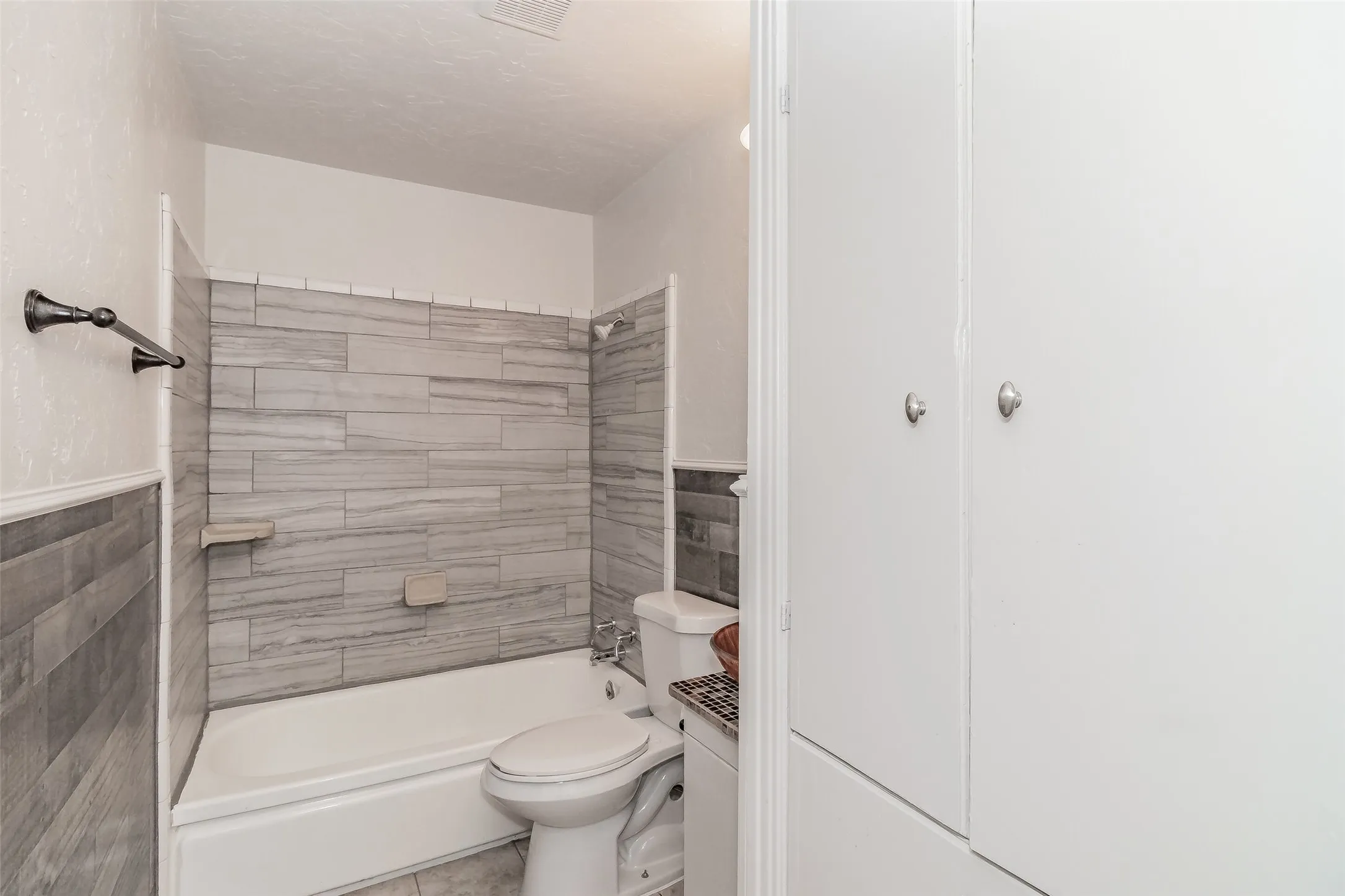Bathtub with gray tile surround, wall-mounted showerhead, and integrated soap dish