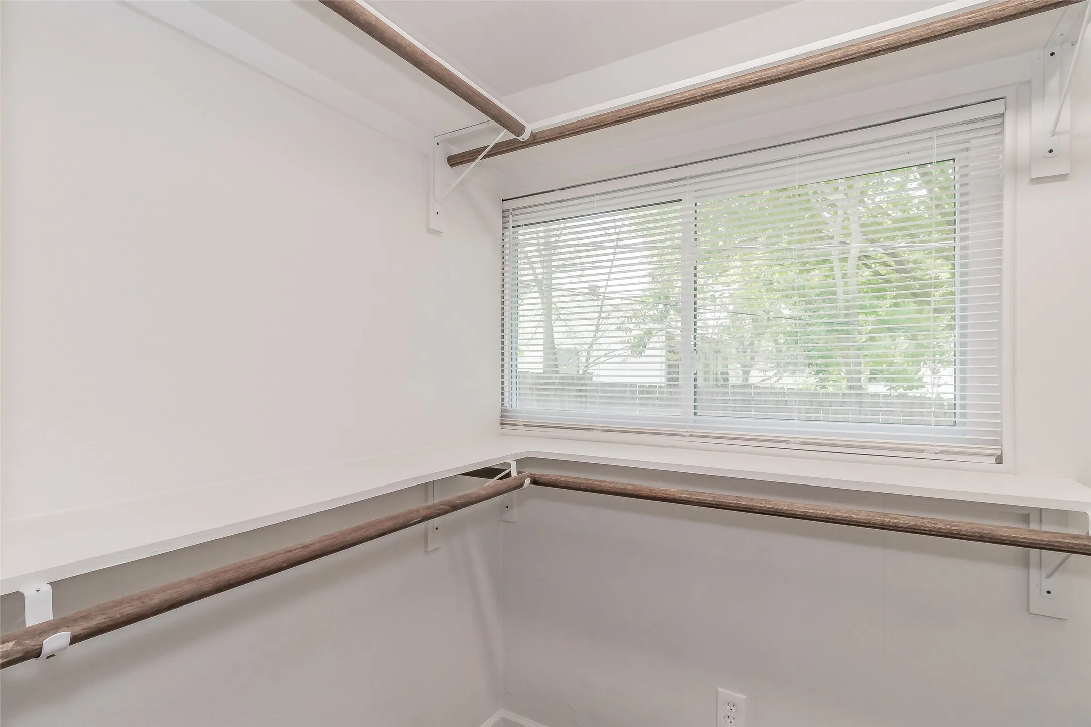 White walls with built-in shelving, integrated hanging rods, and a window with blinds