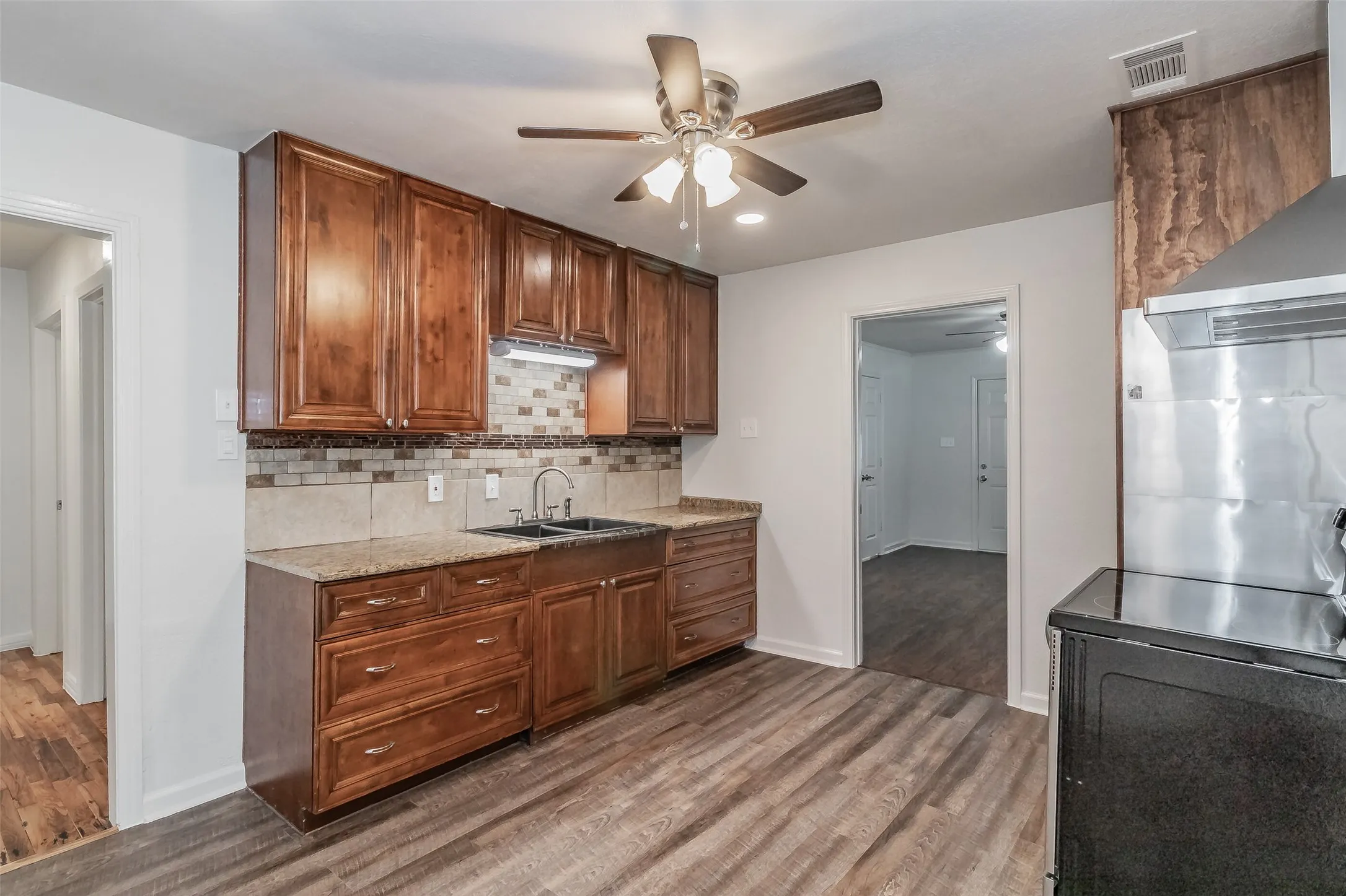 Kitchen featuring wood-finish cabinetry, stone countertops, mosaic tile backsplash, and wood-finish flooring