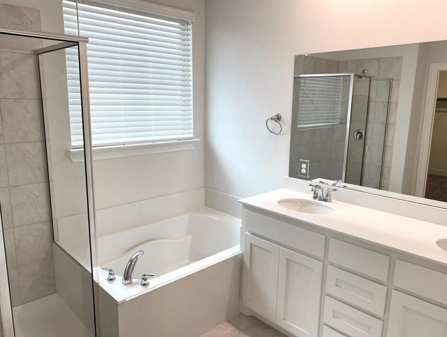 Built-in soaking tub with shower enclosure, single vanity with integrated sink, white shaker-style cabinetry, and a large wall-mounted mirror