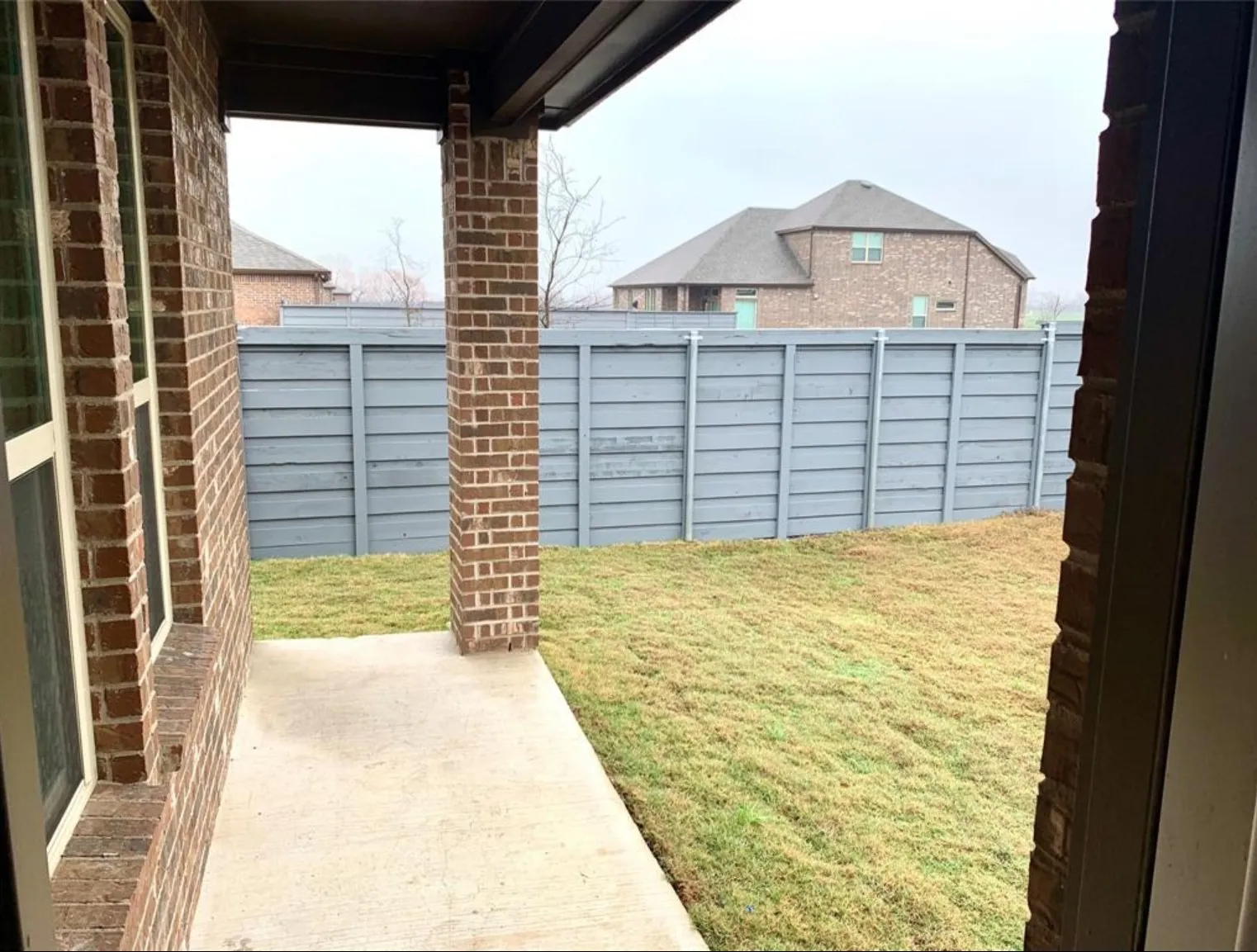 Covered outdoor patio with a concrete surface, brick columns, and a landscaped yard