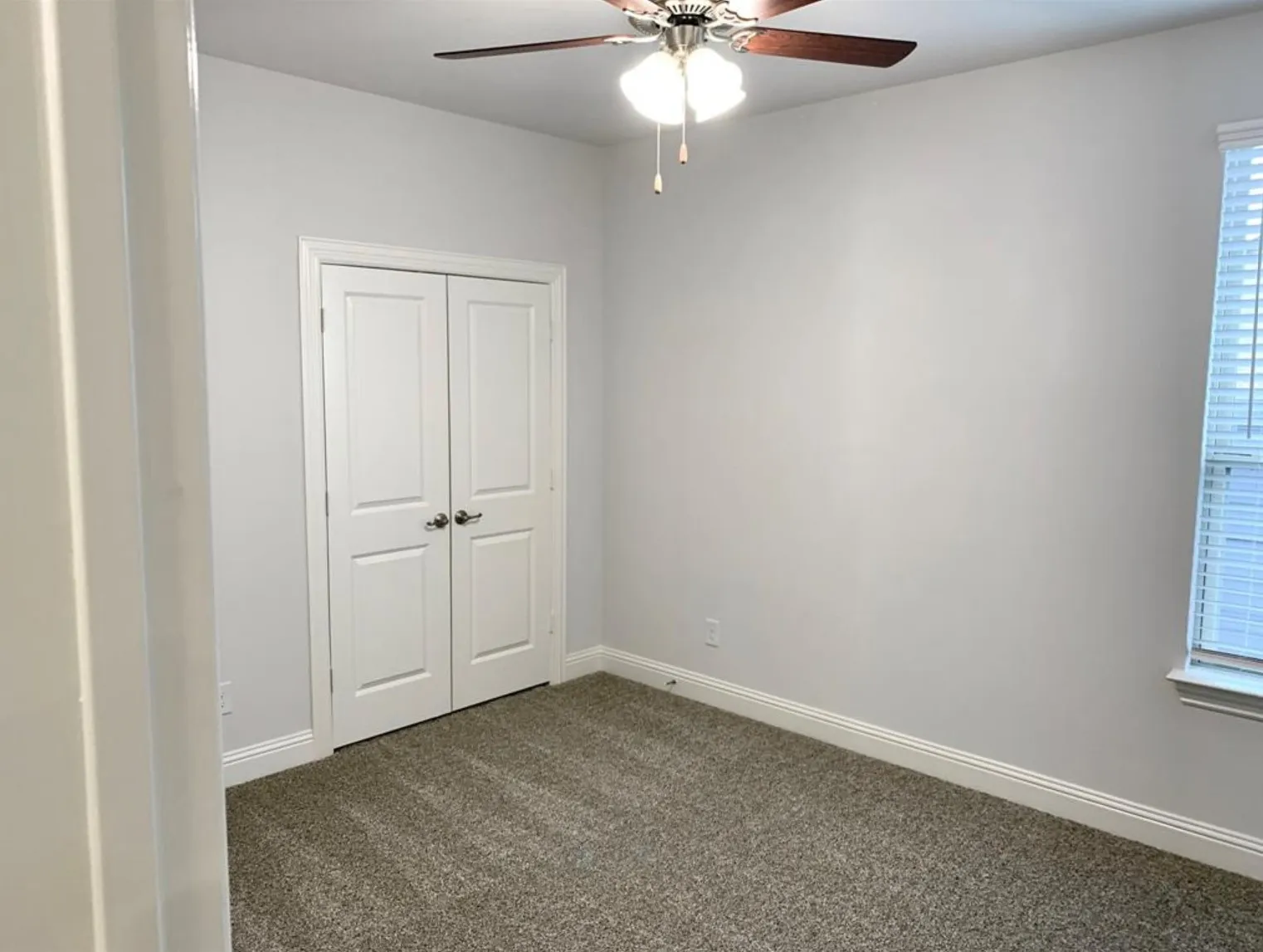 Neutral wall paint, carpet flooring, a ceiling fan with integrated lighting, a window with blinds, and bi-fold doors