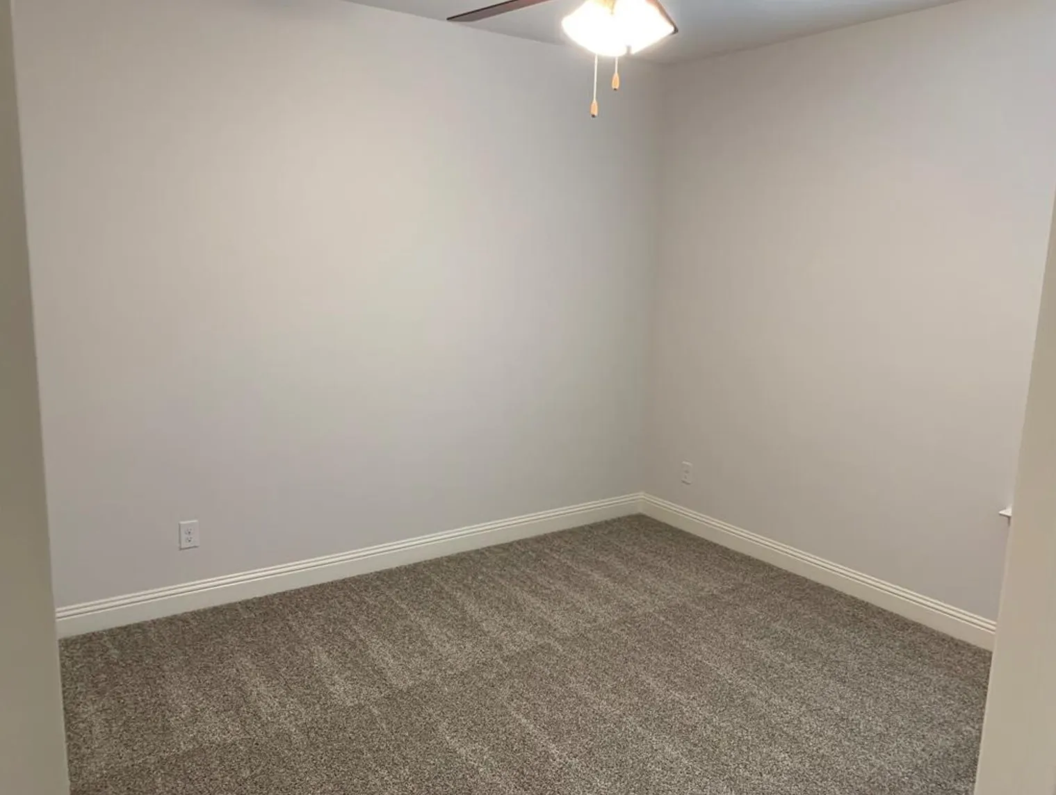 Neutral-toned walls, textured gray carpeting, white trim, and a ceiling fan with integrated lighting