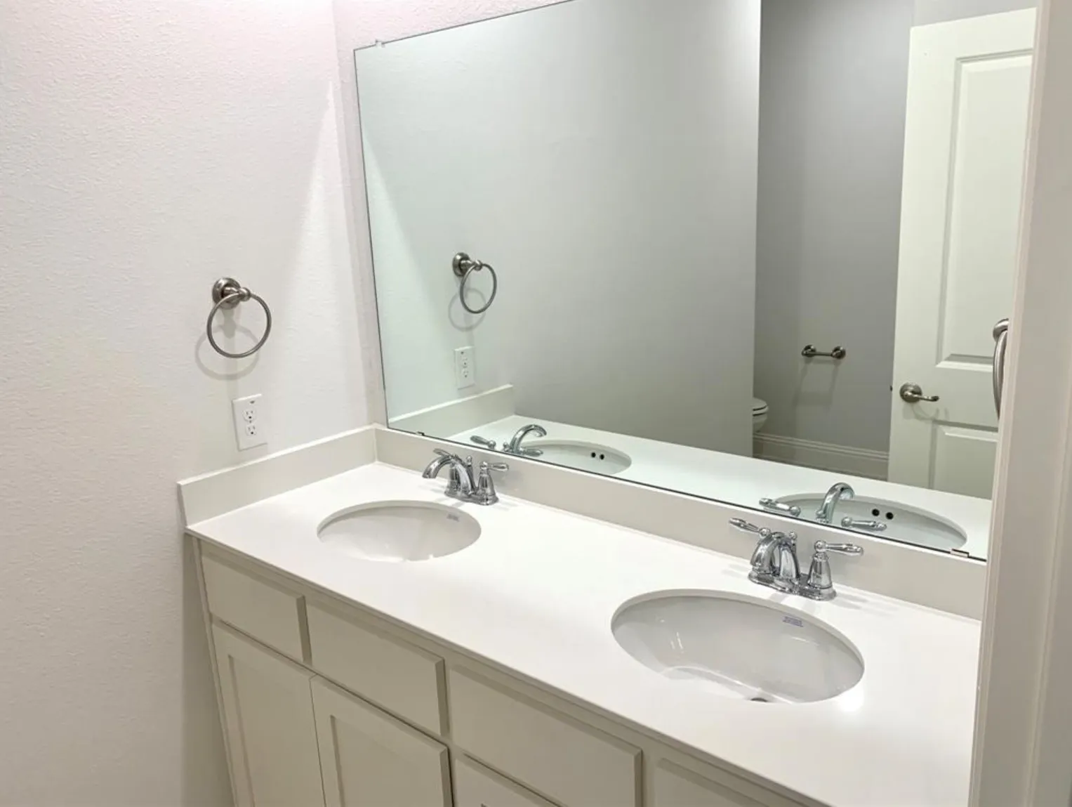 Dual undermount sinks with chrome fixtures, a spacious countertop, and a large wall-mounted mirror