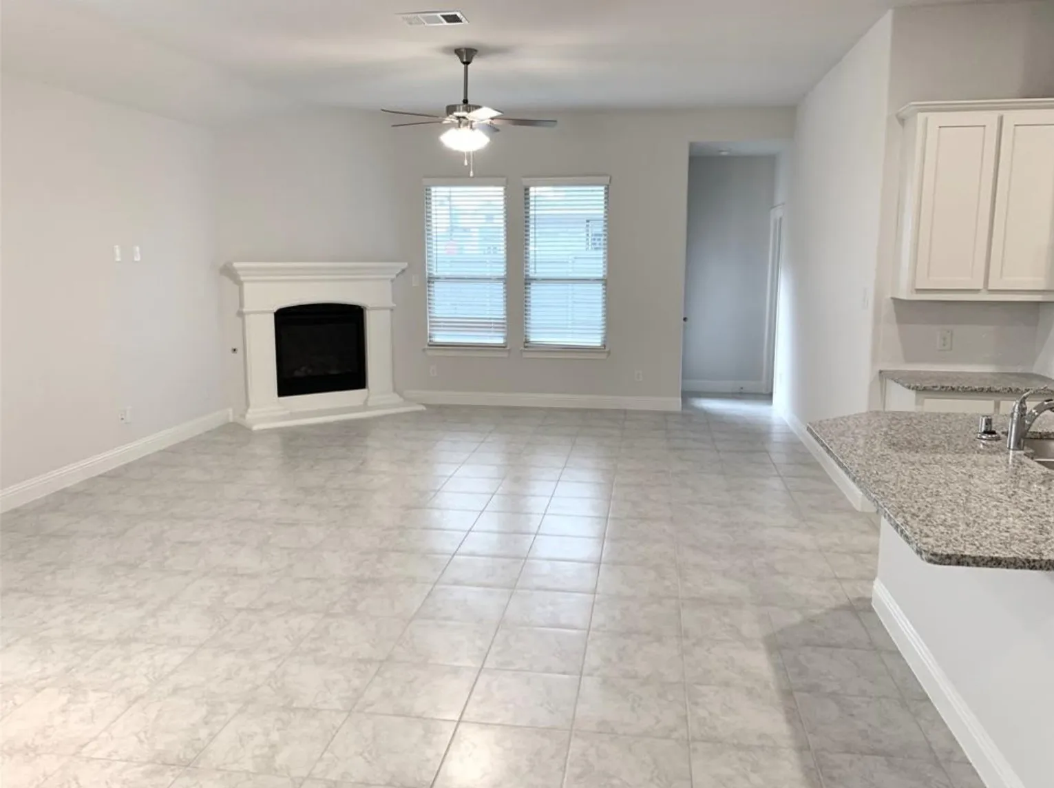 Spacious living area featuring a corner fireplace with a white mantel, tile flooring, and multiple windows with blinds