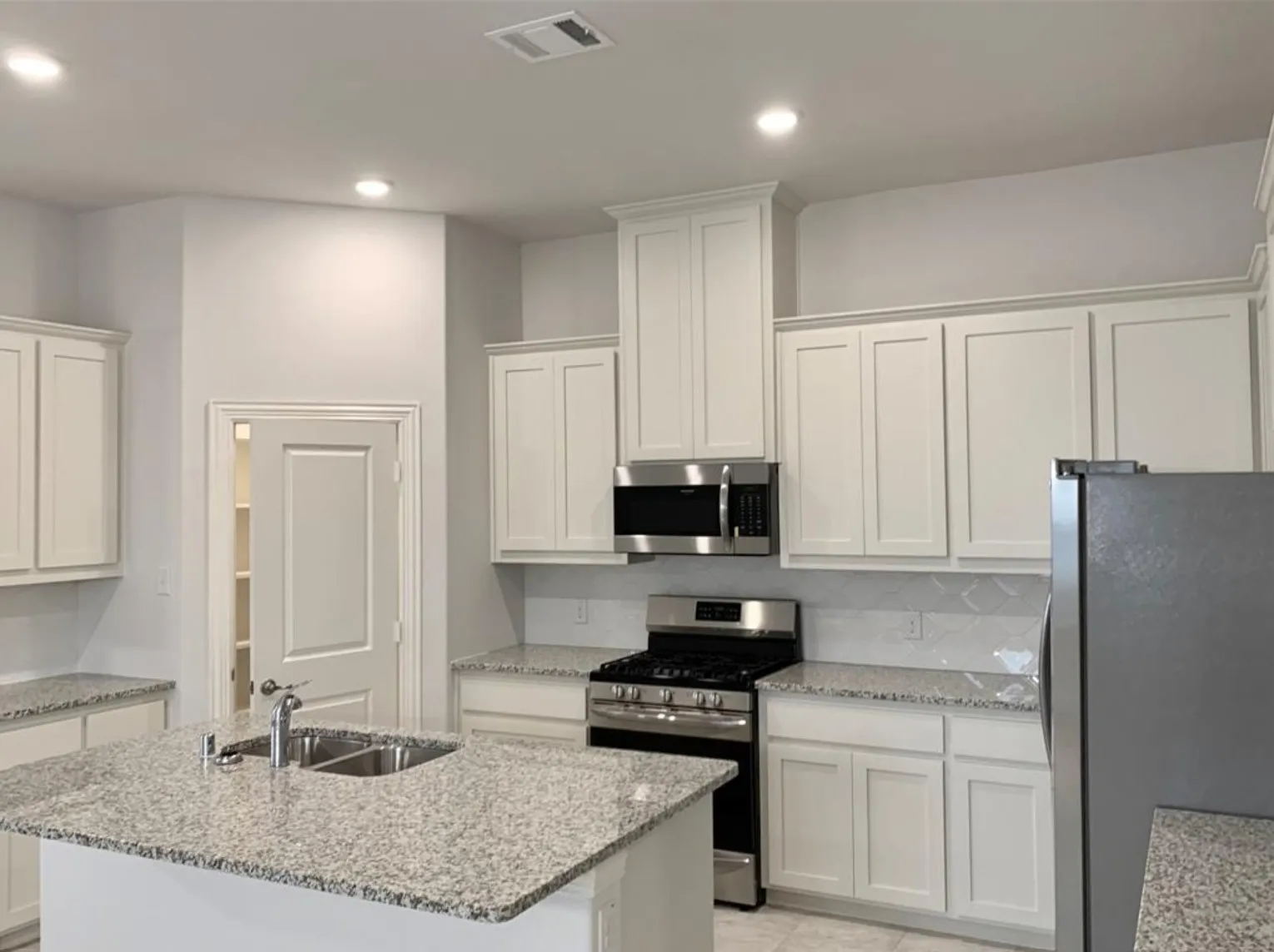 Kitchen featuring a center island, dual basin sink, white cabinetry, integrated microwave, and stainless steel appliances