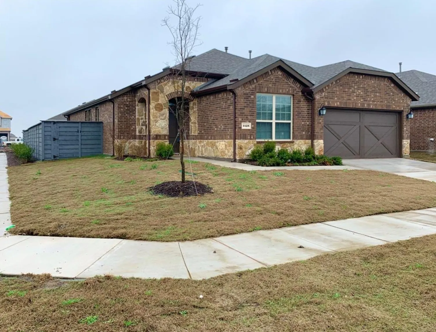 Brick exterior with stone accents, arched entryway, attached garage with decorative doors, and a well-defined front lawn