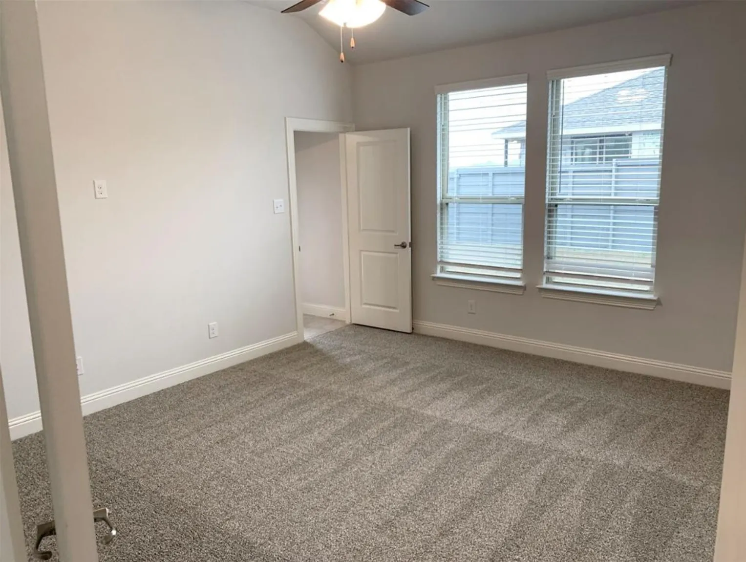 Vaulted ceiling with ceiling fan, two windows with blinds, neutral wall paint, and textured carpet flooring