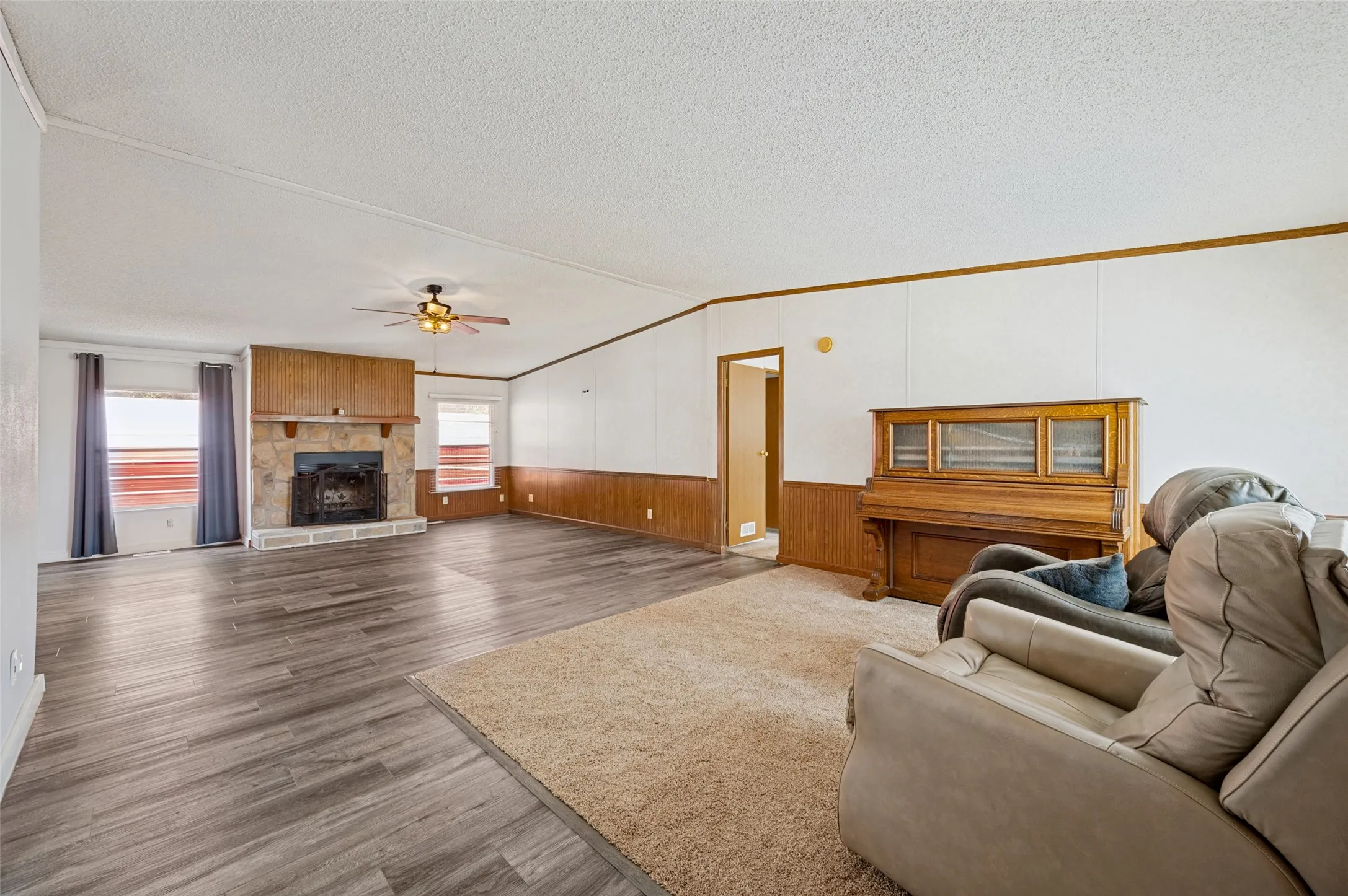 Family Room with vaulted ceilings, wood burning fireplace with stone surround, lvp flooring and ceiling fan.