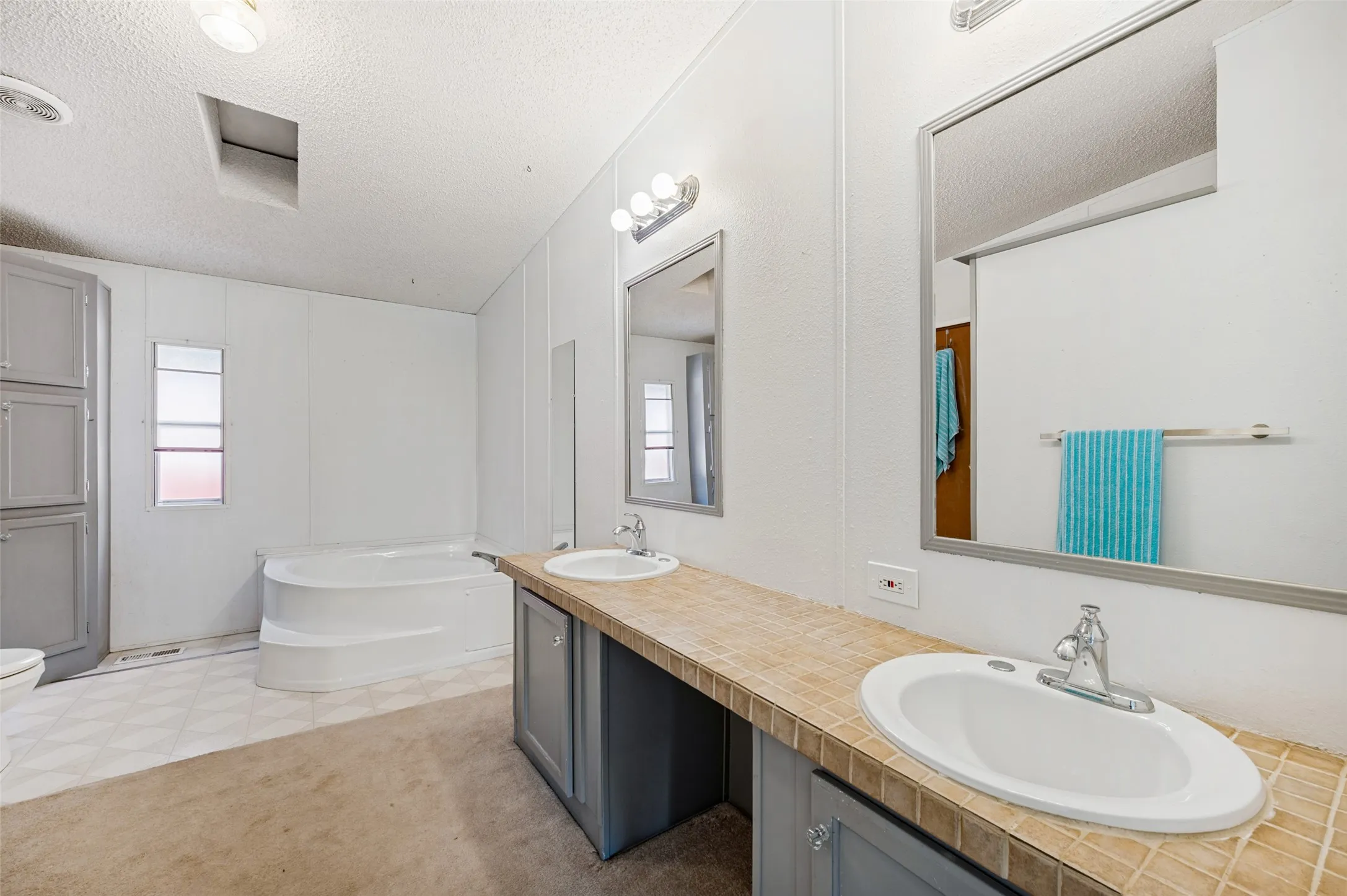 Ensuite primary bathroom features double sinks with tile countertops, large garden tub and separate shower.